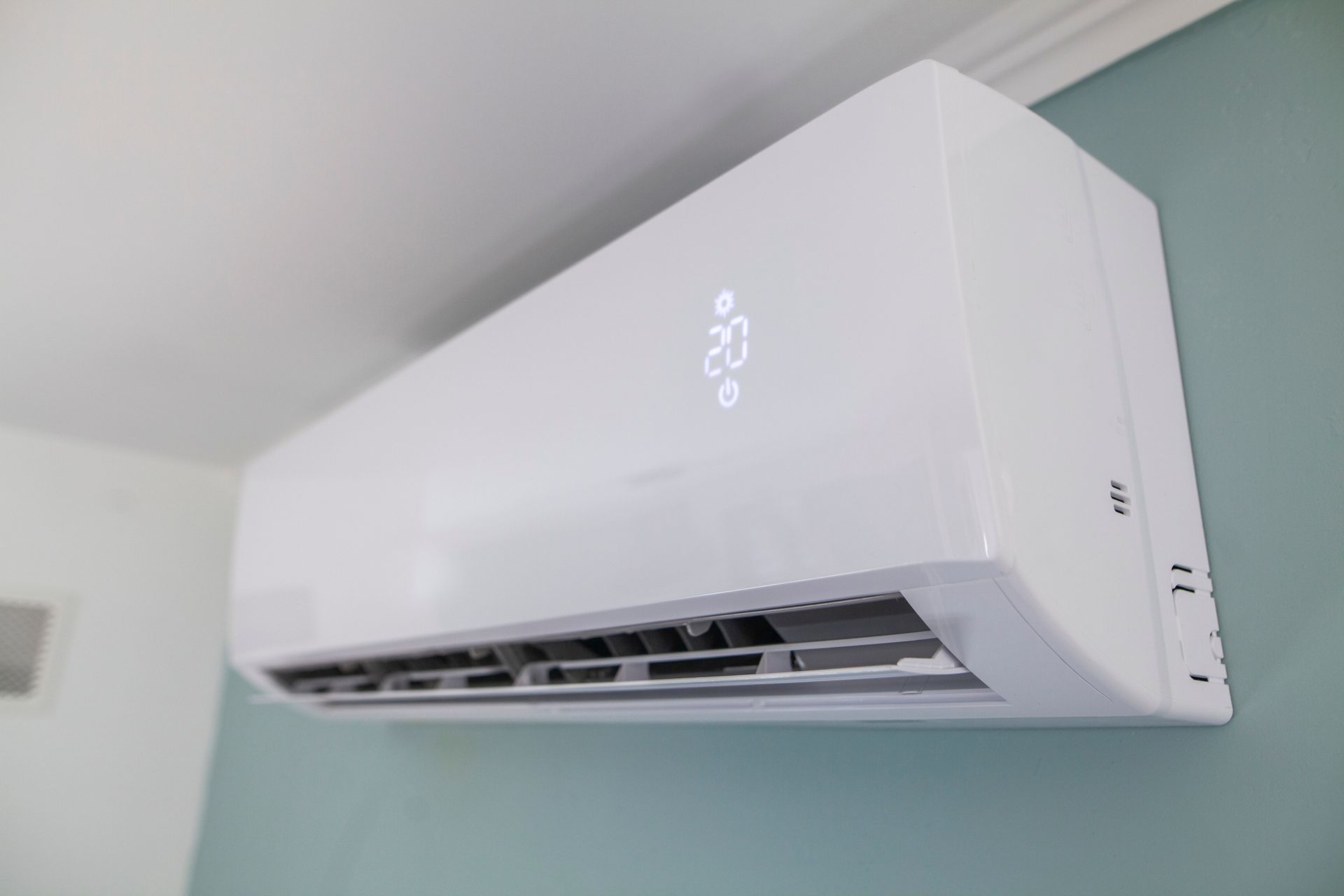 White ductless air conditioner on a teal wall, displaying the temperature as 23.