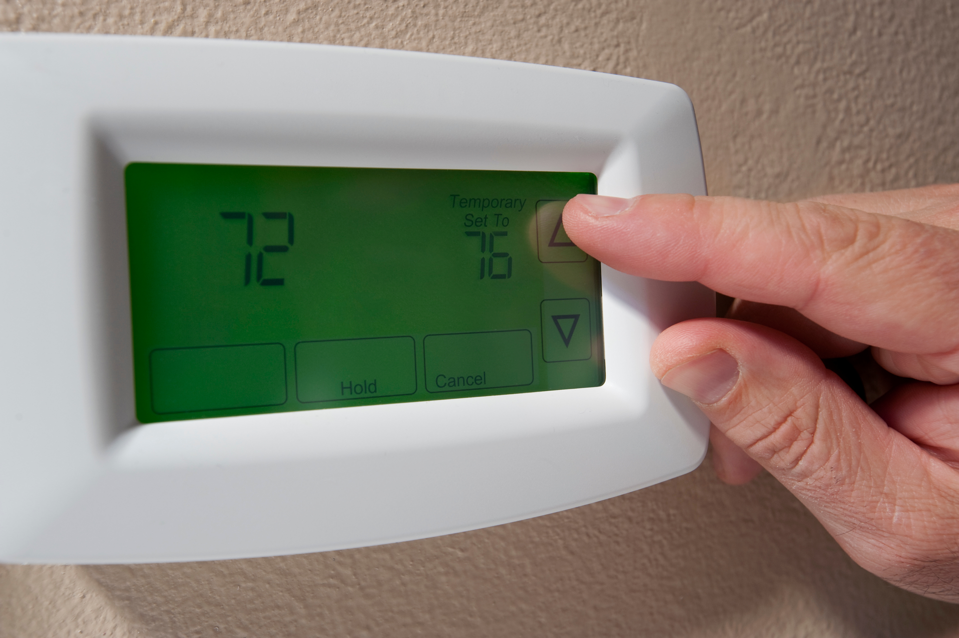 Person adjusting a thermostat, the screen showing 72 degrees and a target of 76 degrees.