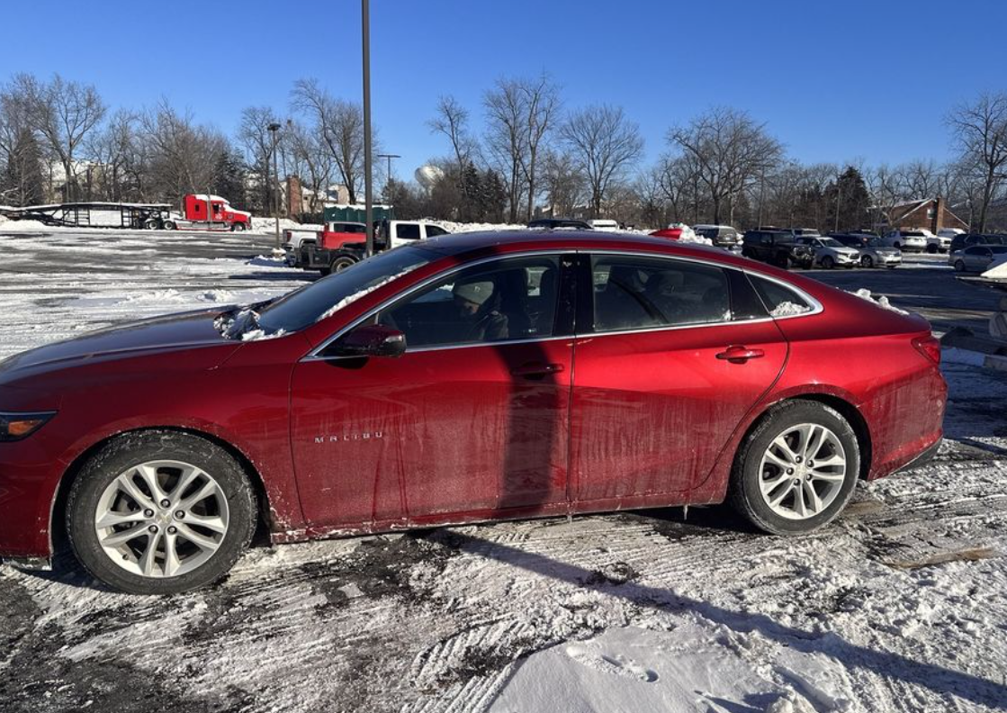 A red car covered in ice in a snowy parking lot.