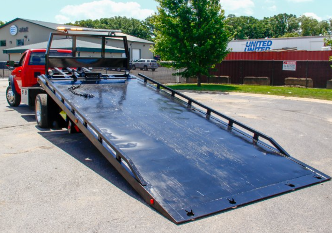 A red flatbed tow truck in a parking lot on a sunny day.
