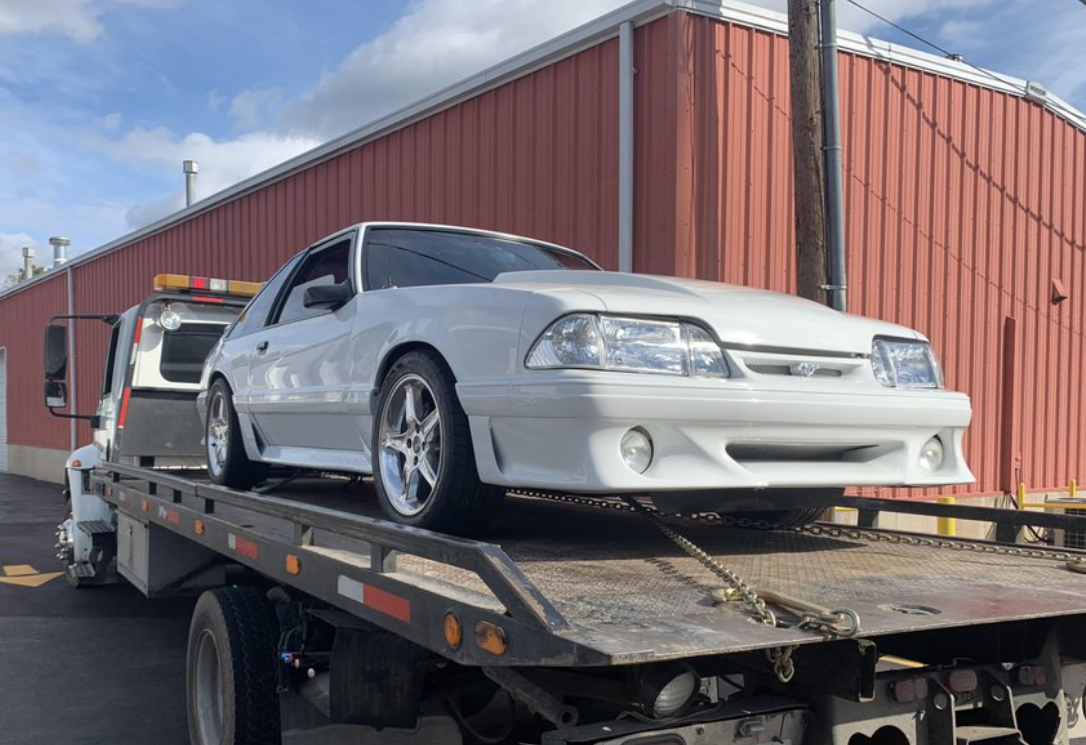 A white car being towed onto a flatbed tow truck on a road, sunny day.