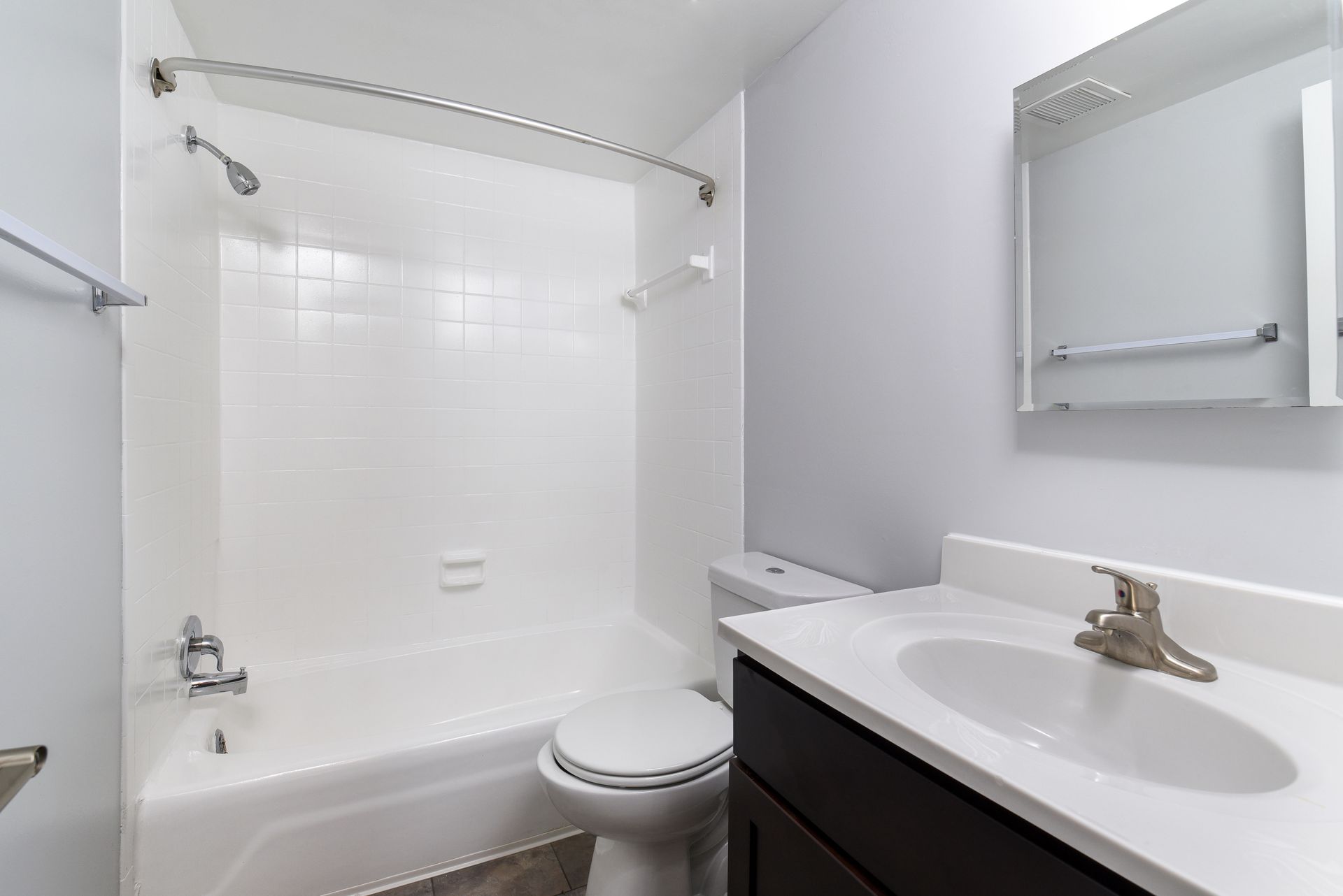 Bathroom with white tub, toilet, and sink, light grey walls, and a silver faucet at Glenmont Station in Silver Spring, MD.