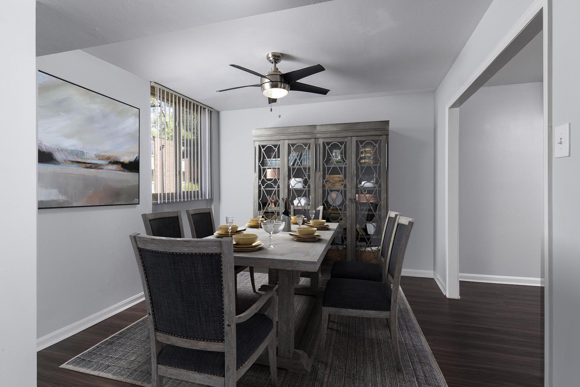 Dining room with a table set for a meal, large china cabinet, and artwork at Glenmont Station in Silver Spring, MD.