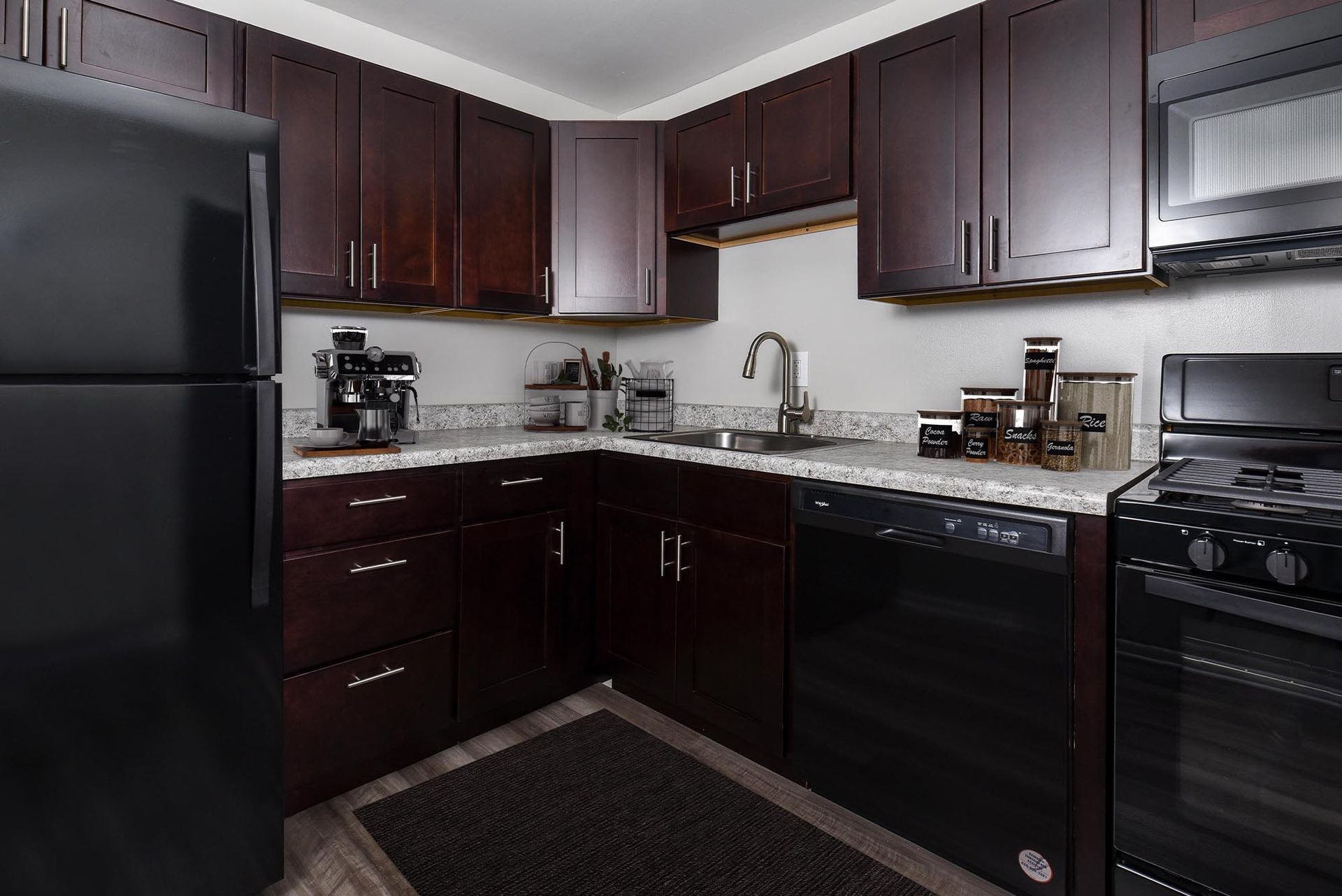 Kitchen with dark brown cabinets, black appliances, and granite countertops at Glenmont Station in Silver Spring, MD.