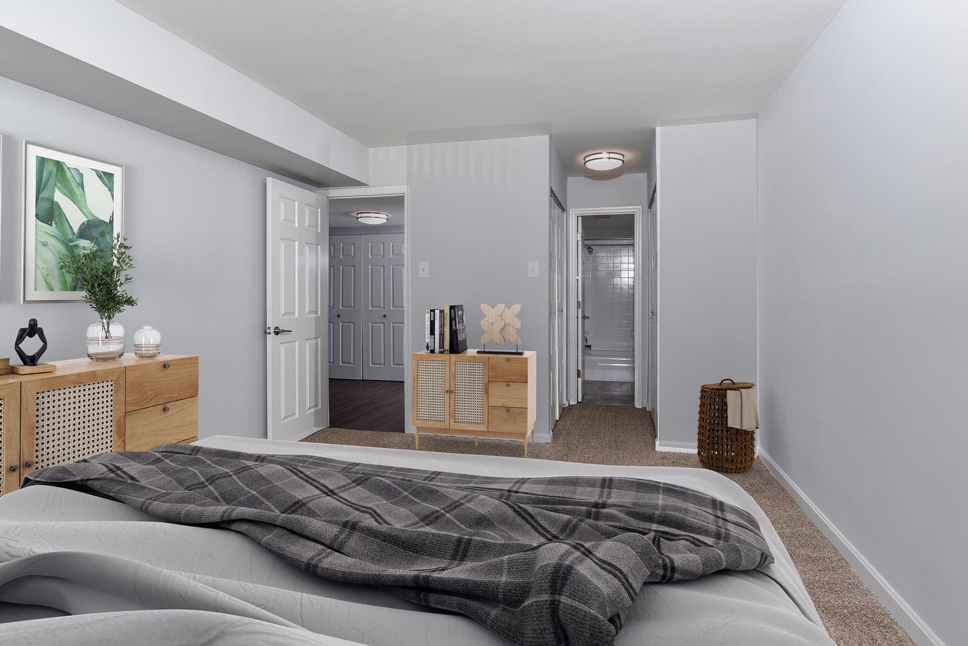 Bedroom with bed, wooden dressers, and access to a bathroom and hallway at Glenmont Station in Silver Spring, MD.