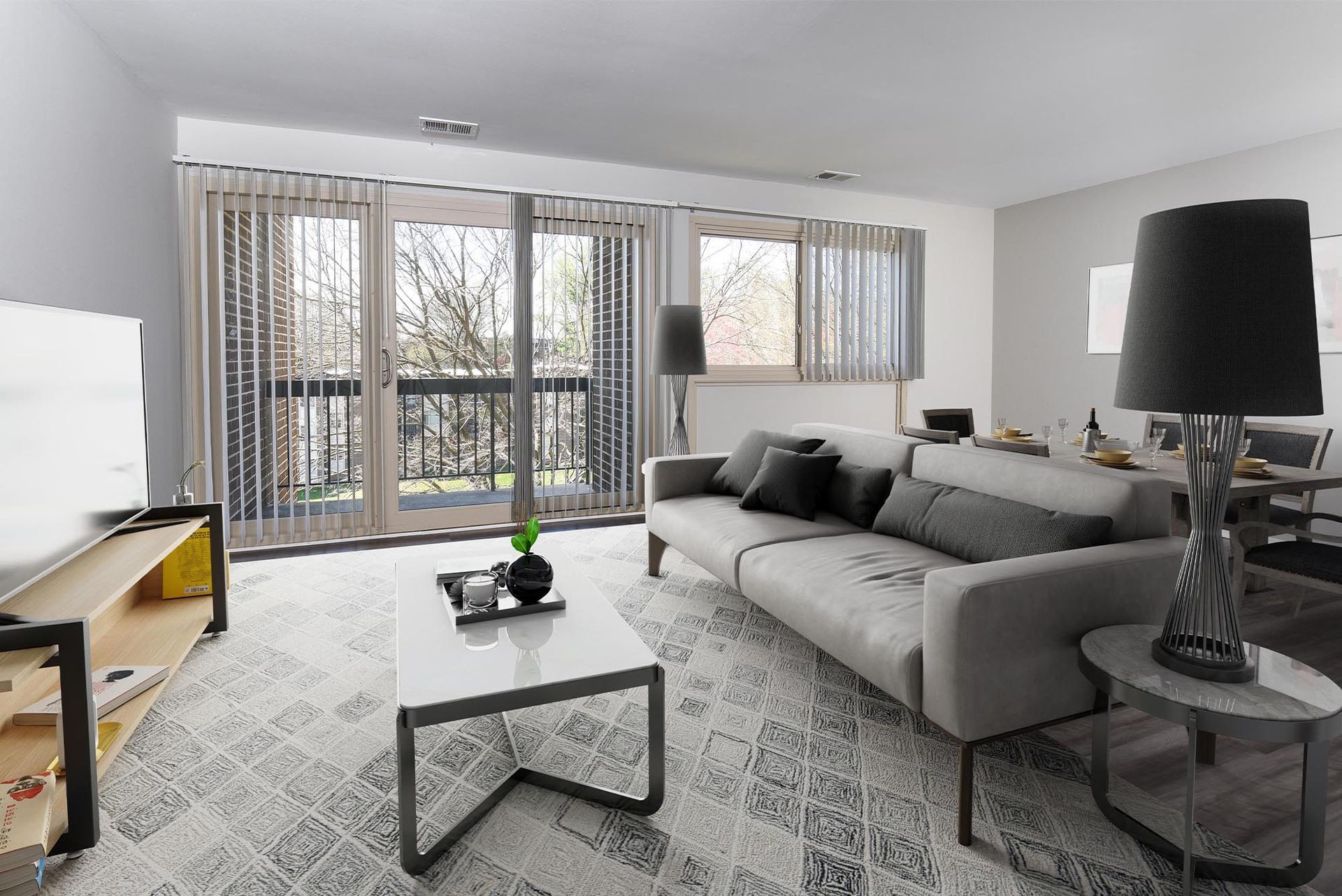 Living room with gray sofa, coffee table, rug, balcony, and large windows at Glenmont Station in Silver Spring, MD.