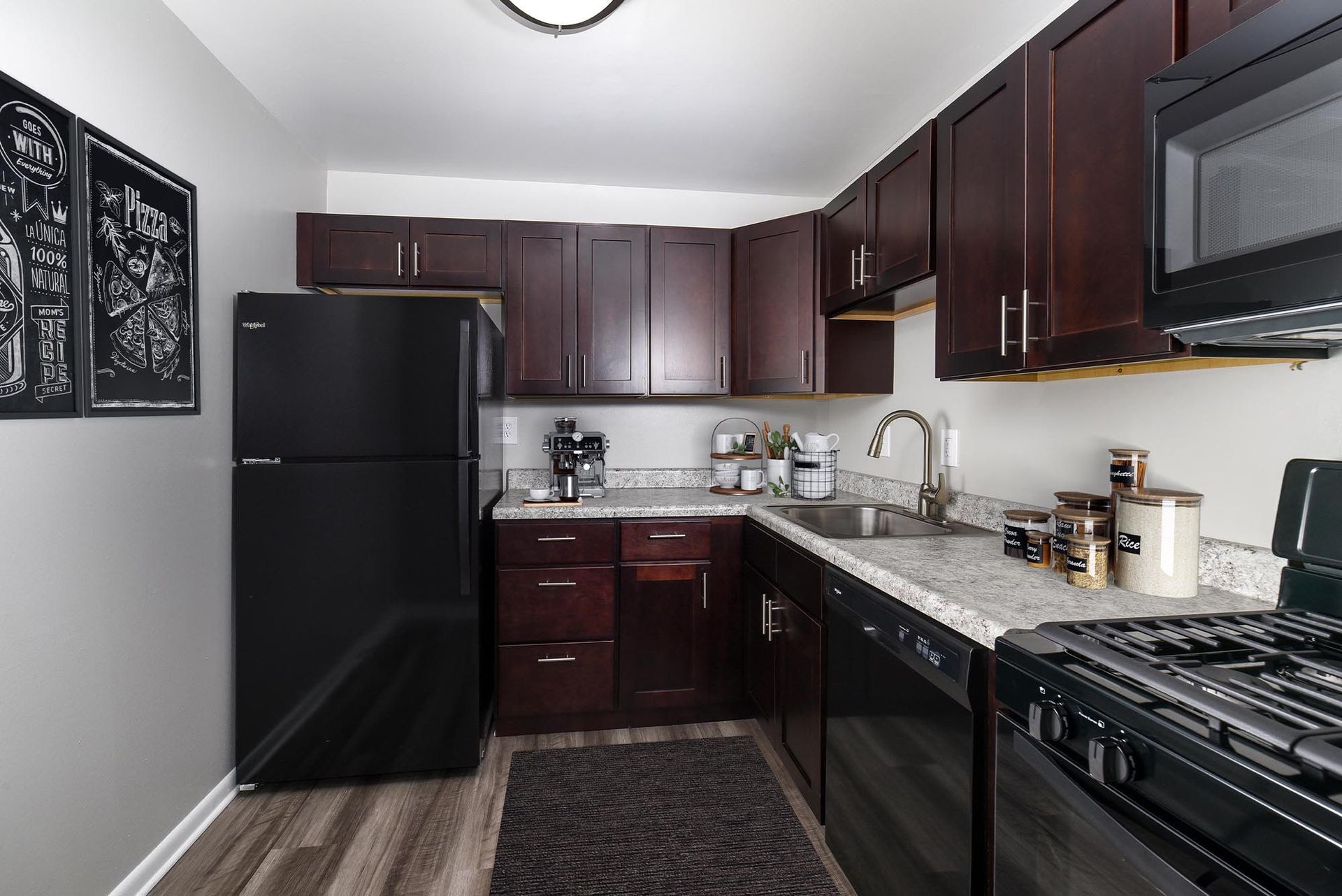 Kitchen with dark cabinets, black appliances, light countertop, gray walls, and wood-look flooring at Landmark at Glenmont Station in Silver Spring, MD.