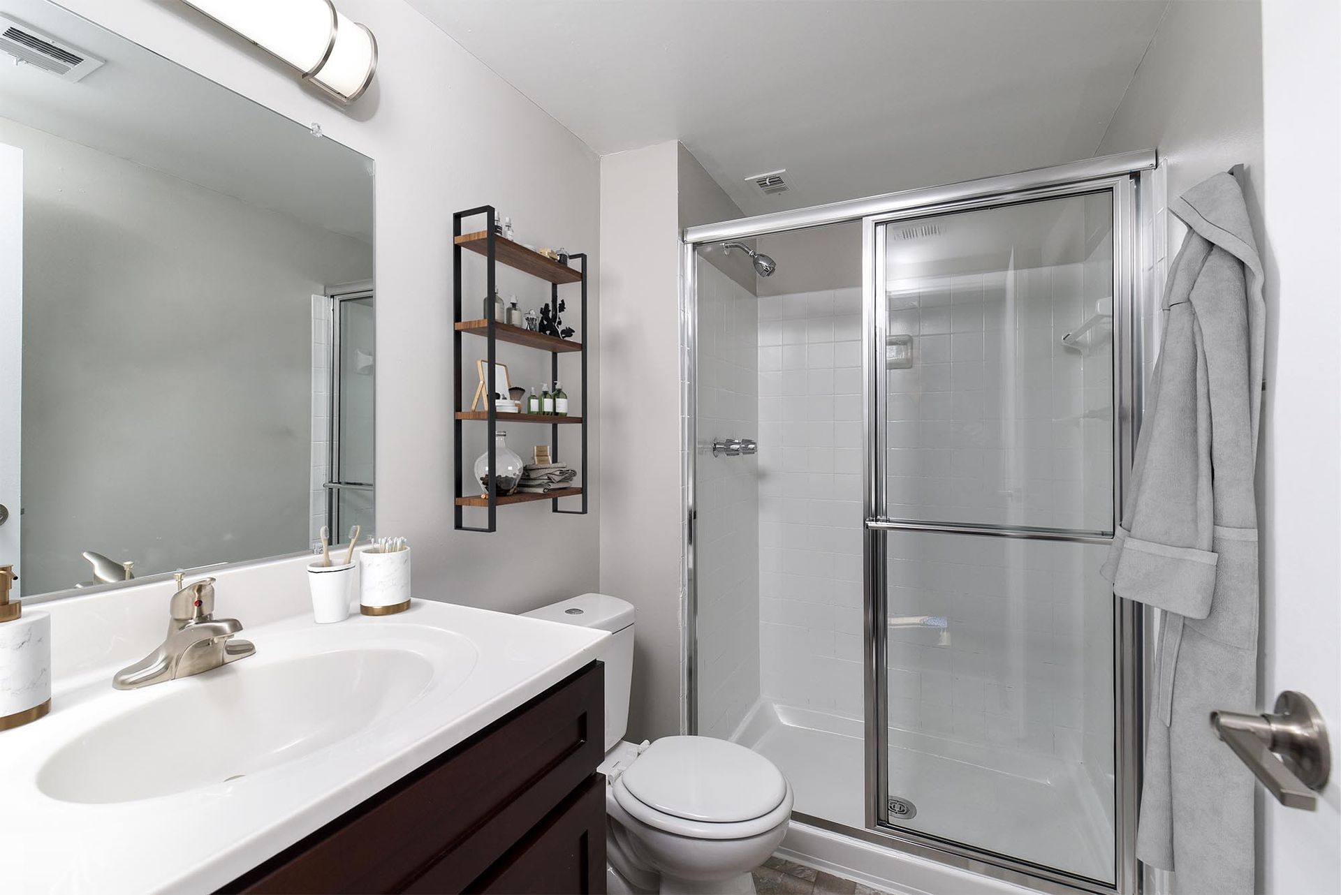Modern bathroom with a white shower, toilet, and sink, with a dark wooden vanity at Glenmont Station in Silver Spring, MD.
