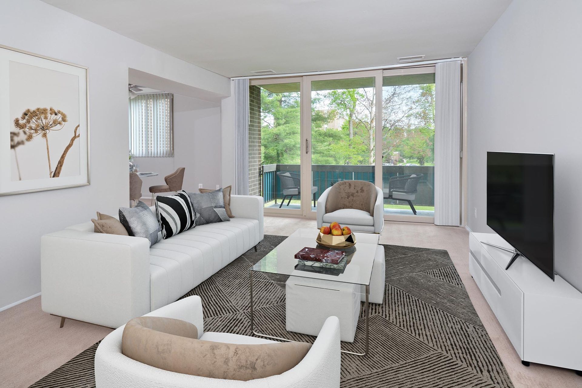 Modern living room with white furniture, large window to a balcony, and a TV at Glenmont Station in Silver Spring, MD.