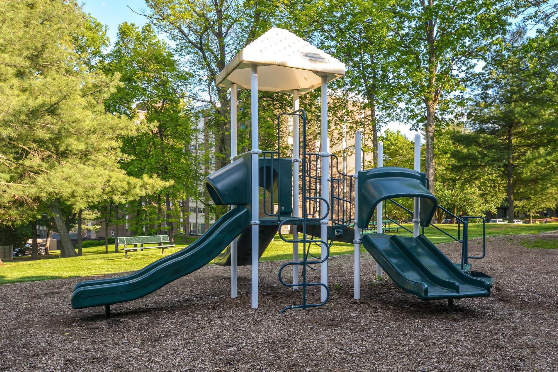 Playground with green slides, climbing structure, and trees at Glenmont Station in Silver Spring, MD.