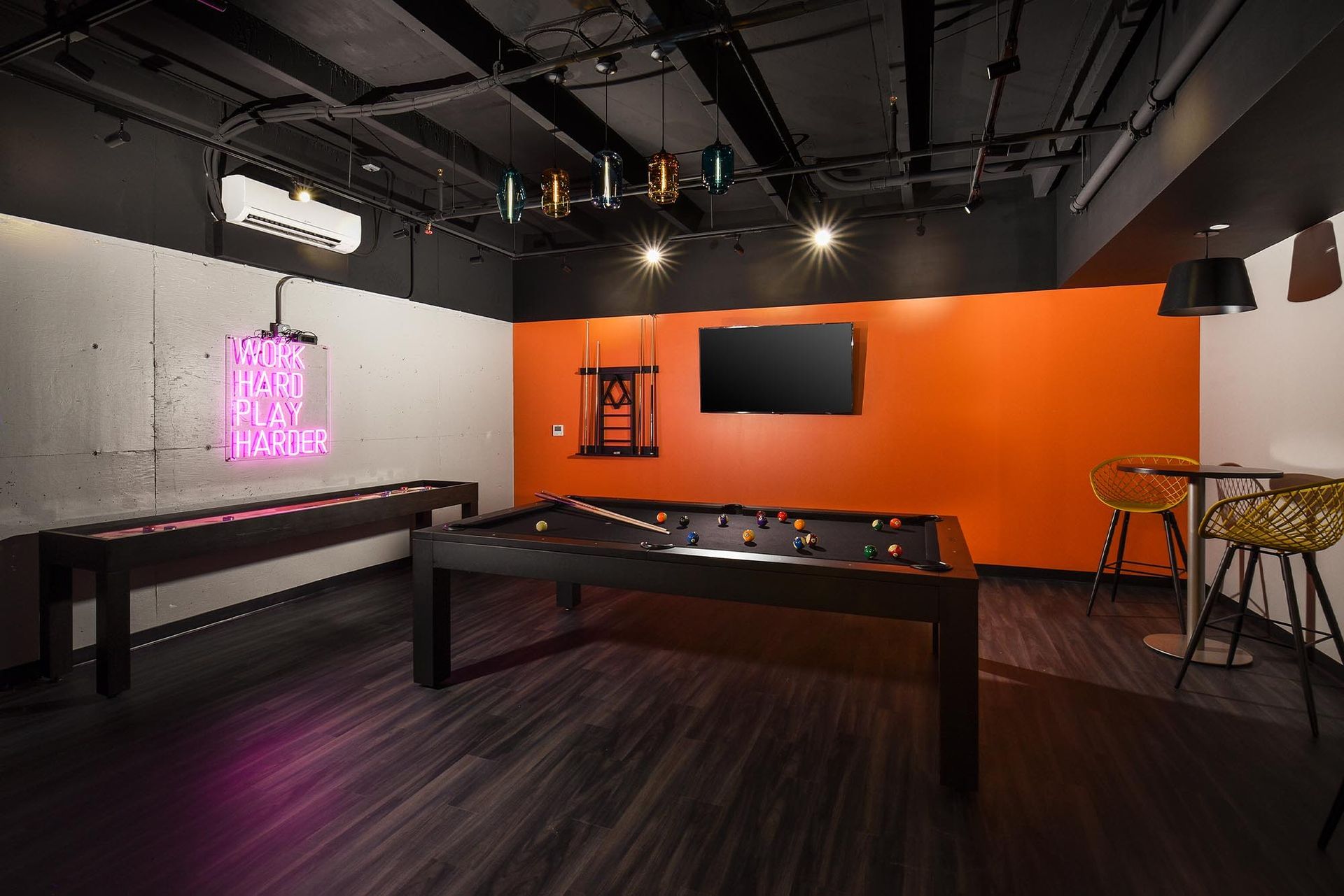 Game room with pool table, air hockey, orange accent wall, and bar seating at Glenmont Station in Silver Spring, MD.