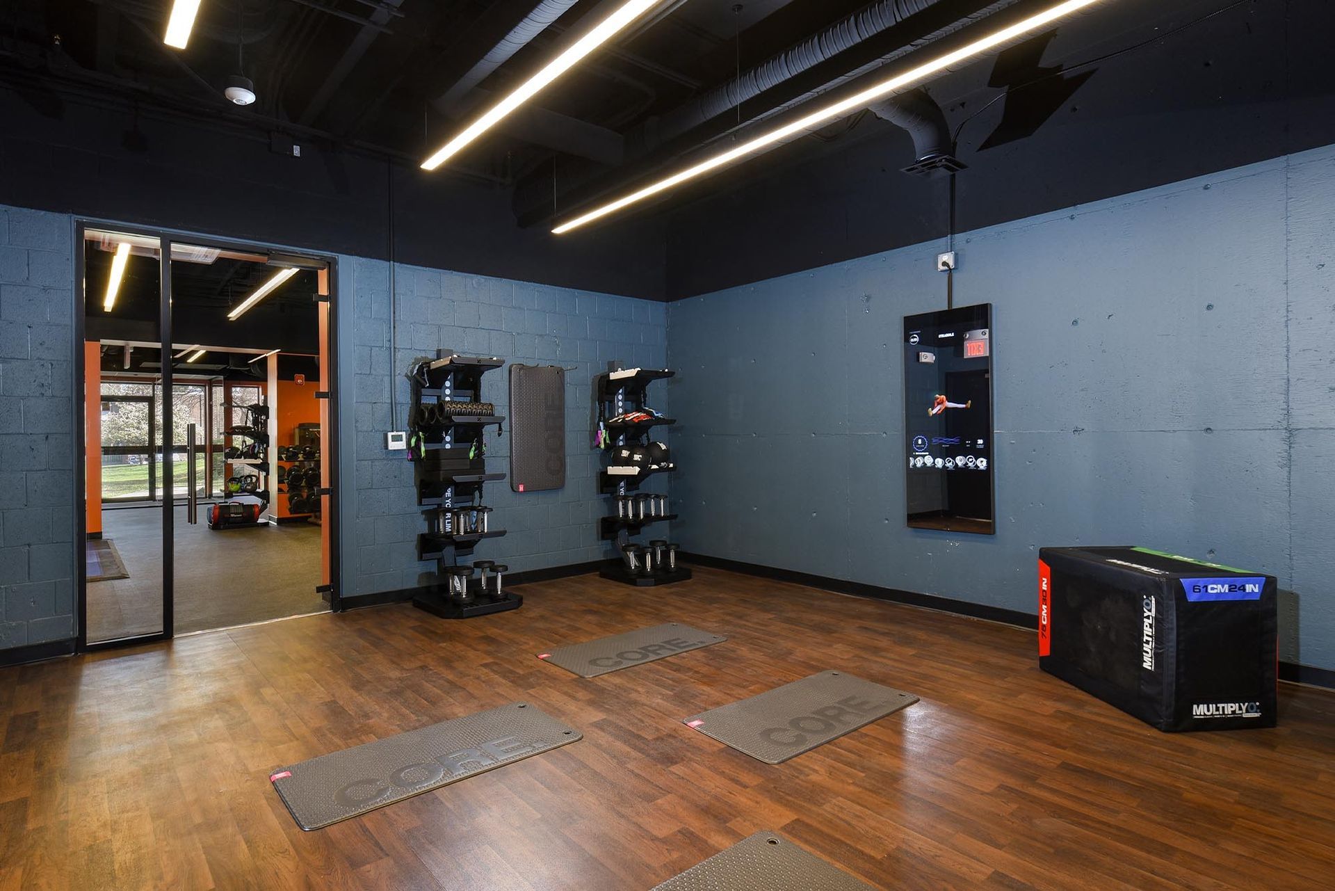 Gym interior with workout equipment and mats on a wooden floor. Dark blue walls, black ceiling, and open doorway at Glenmont Station in Silver Spring, MD.