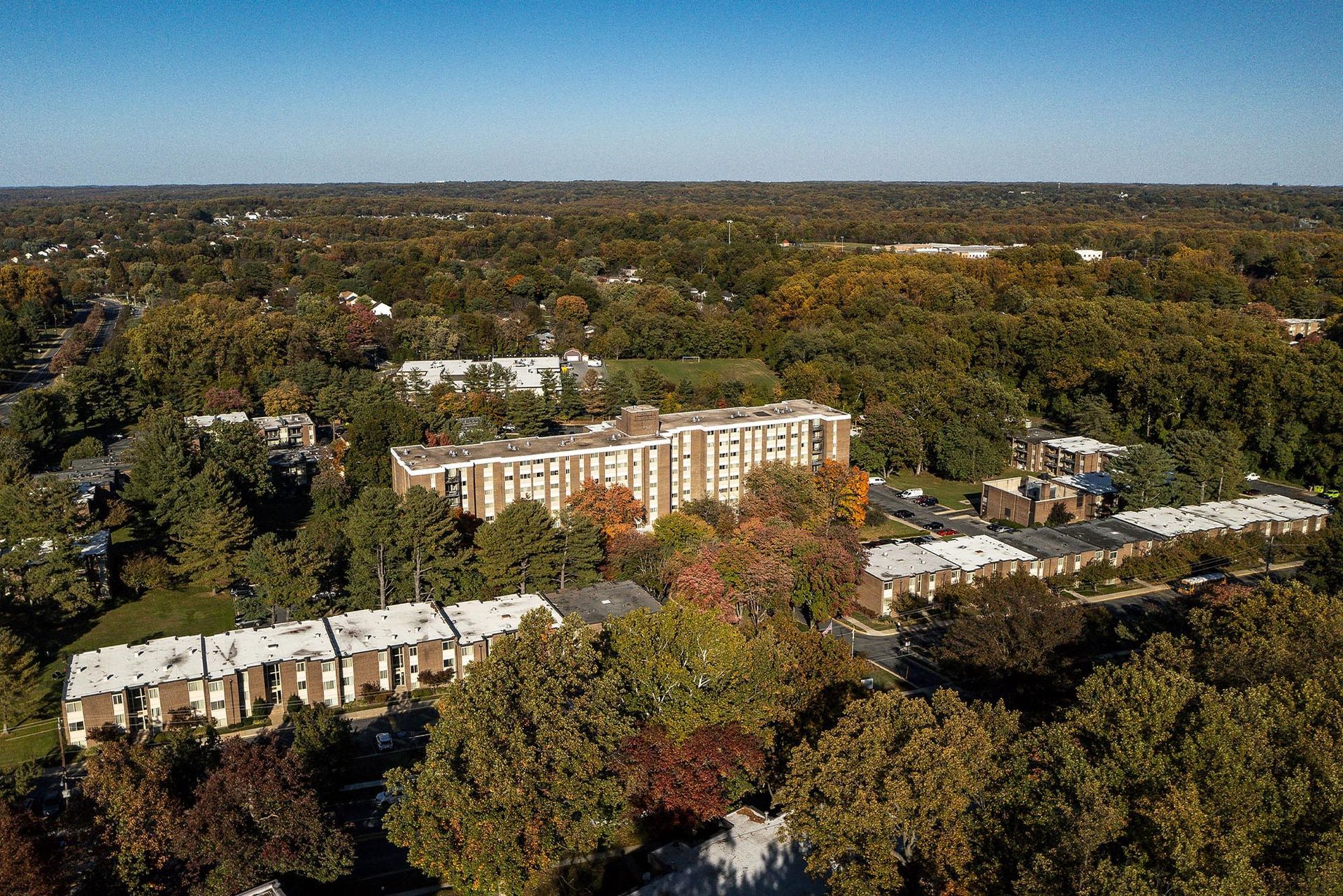 Aerial view of a multistory apartment building and townhouses surrounded by trees under a clear sky at Glenmont Station in Silver Spring, MD.