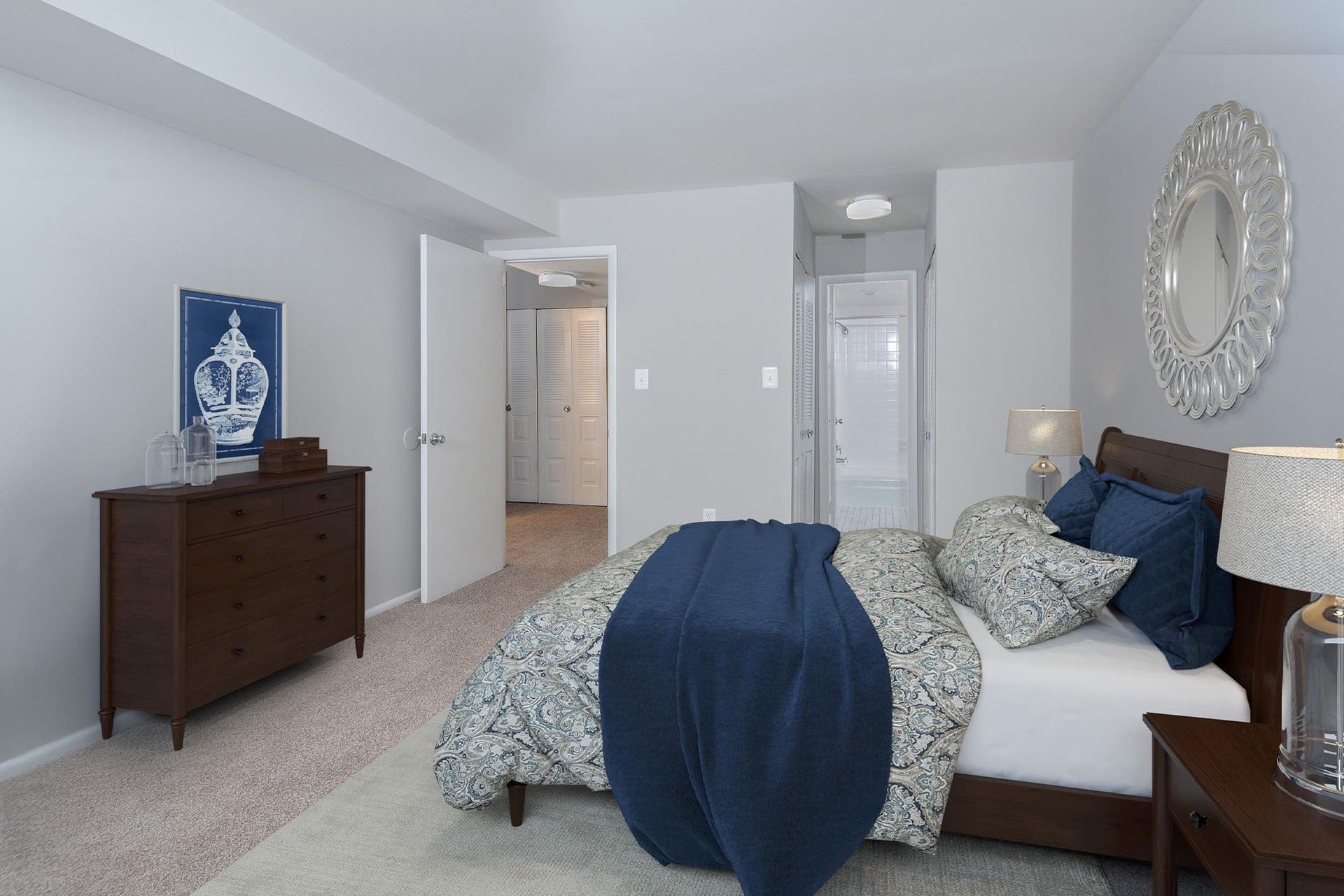 Bedroom with bed, dresser, open doorway, and decorative mirror at Glenmont Station in Silver Spring, MD.
