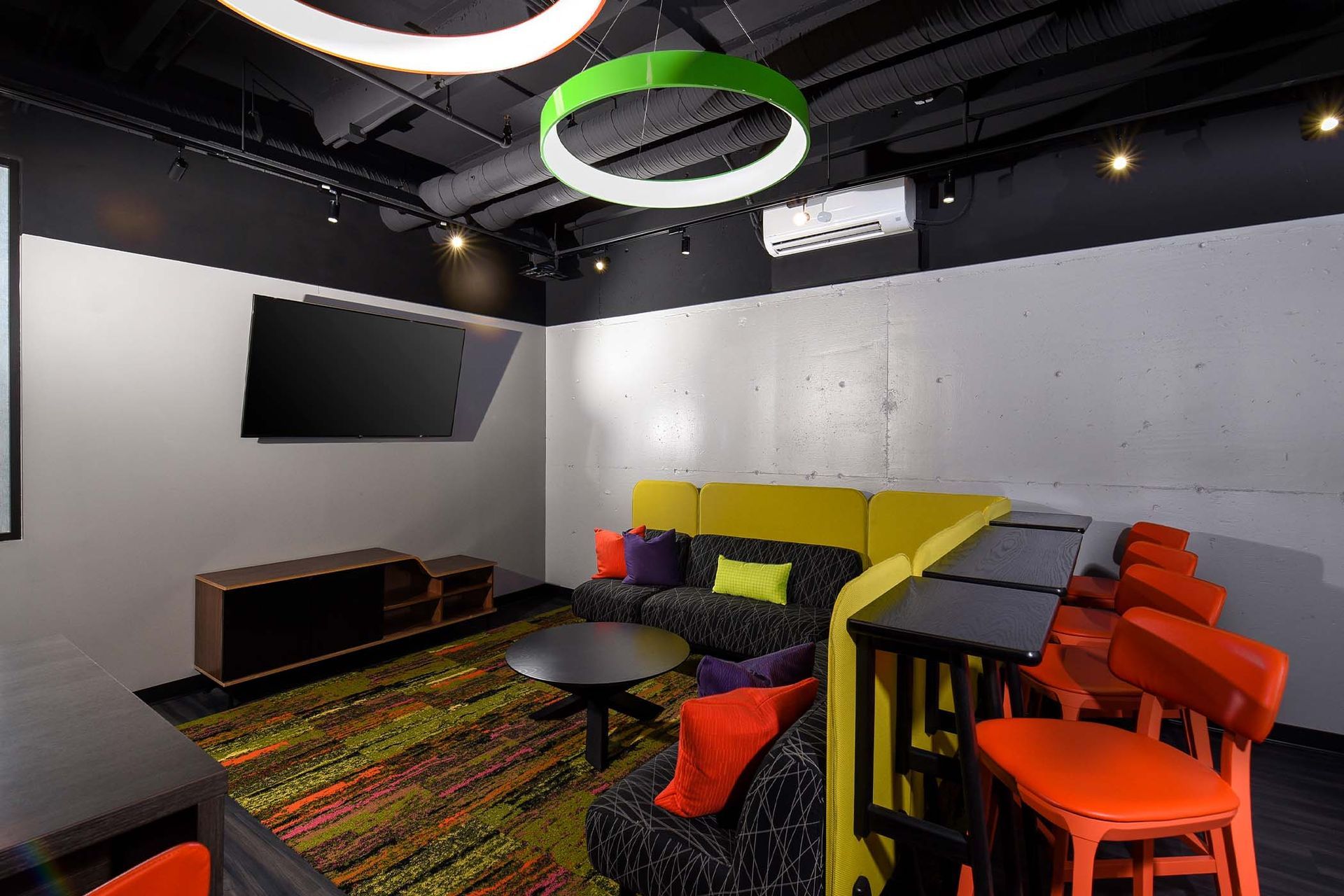 Modern lounge area with colorful furniture, TV, and decorative lighting at Glenmont Station in Silver Spring, MD.