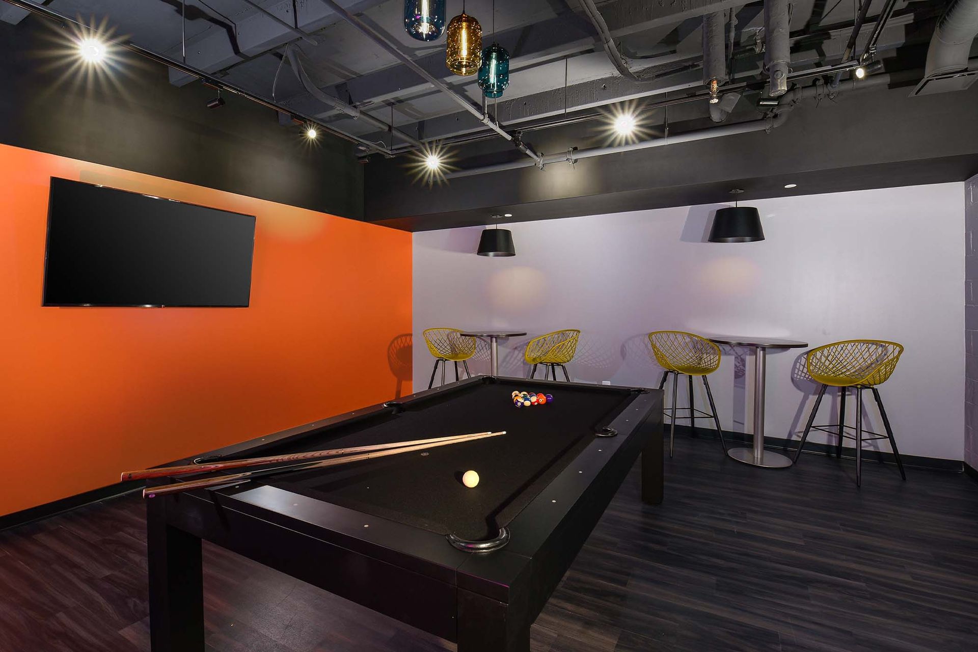 Pool table in a room with orange and white walls, black ceiling, and bar-style seating at Glenmont Station in Silver Spring, MD.