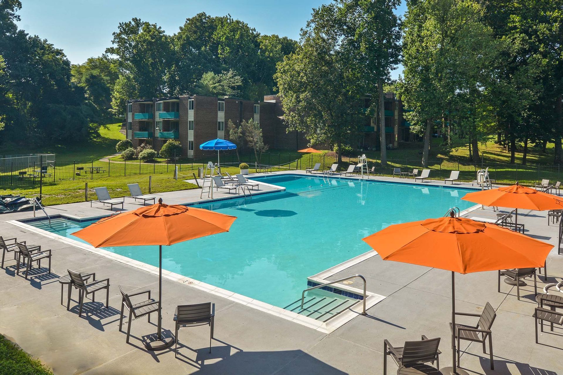 Swimming pool with orange umbrellas and lounge chairs, surrounded by trees and a brick building at Glenmont Station in Silver Spring, MD.
