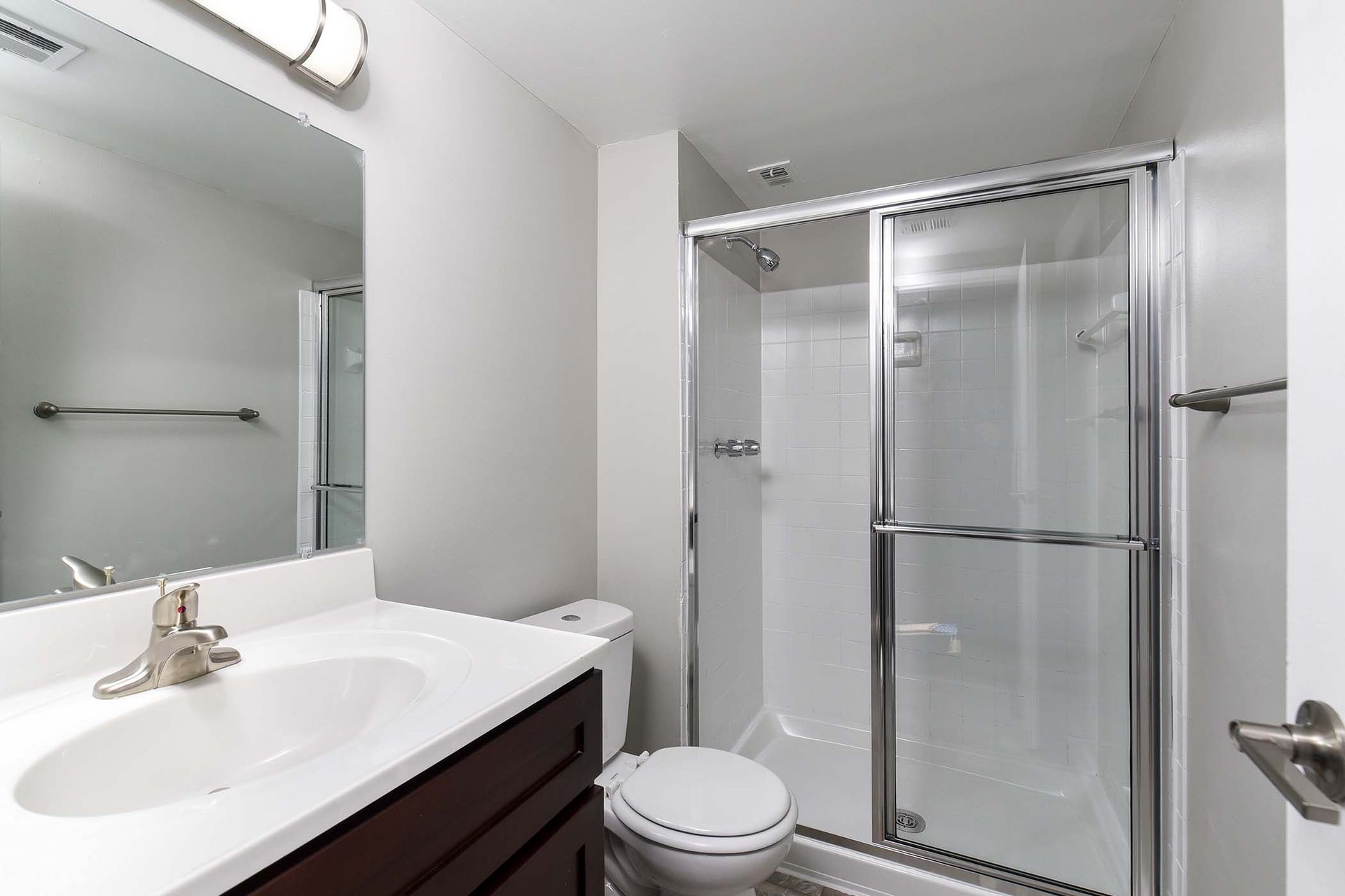Bathroom with white walls, a vanity, toilet, and a glass shower enclosure at Glenmont Station in Silver Spring, MD.