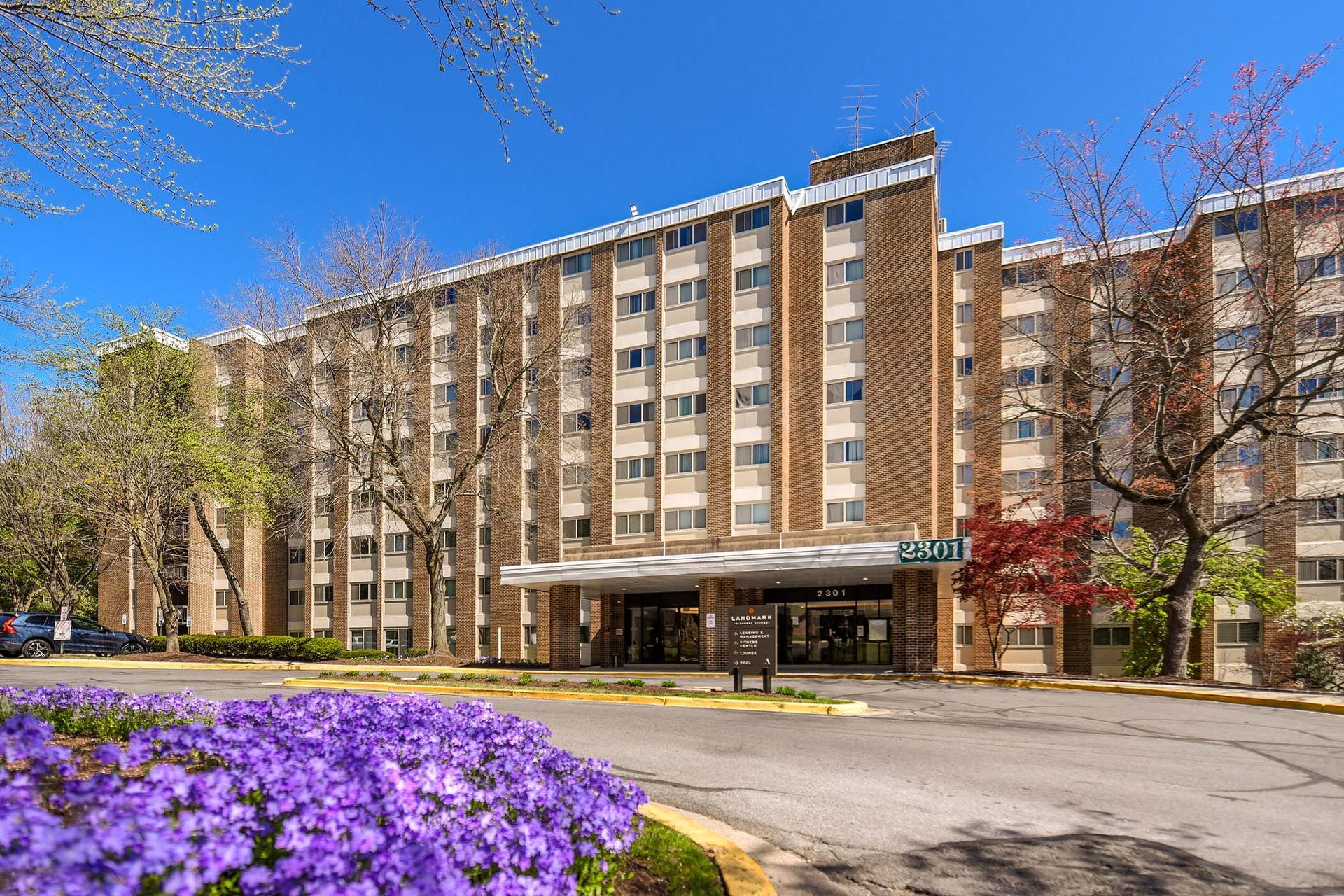 Large brick building with a covered entrance, purple flowers in the foreground, and a blue sky at Glenmont Station in Silver Spring, MD.