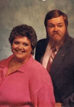 Couple posing for a portrait. Woman in pink shirt smiles, man with long beard in suit.