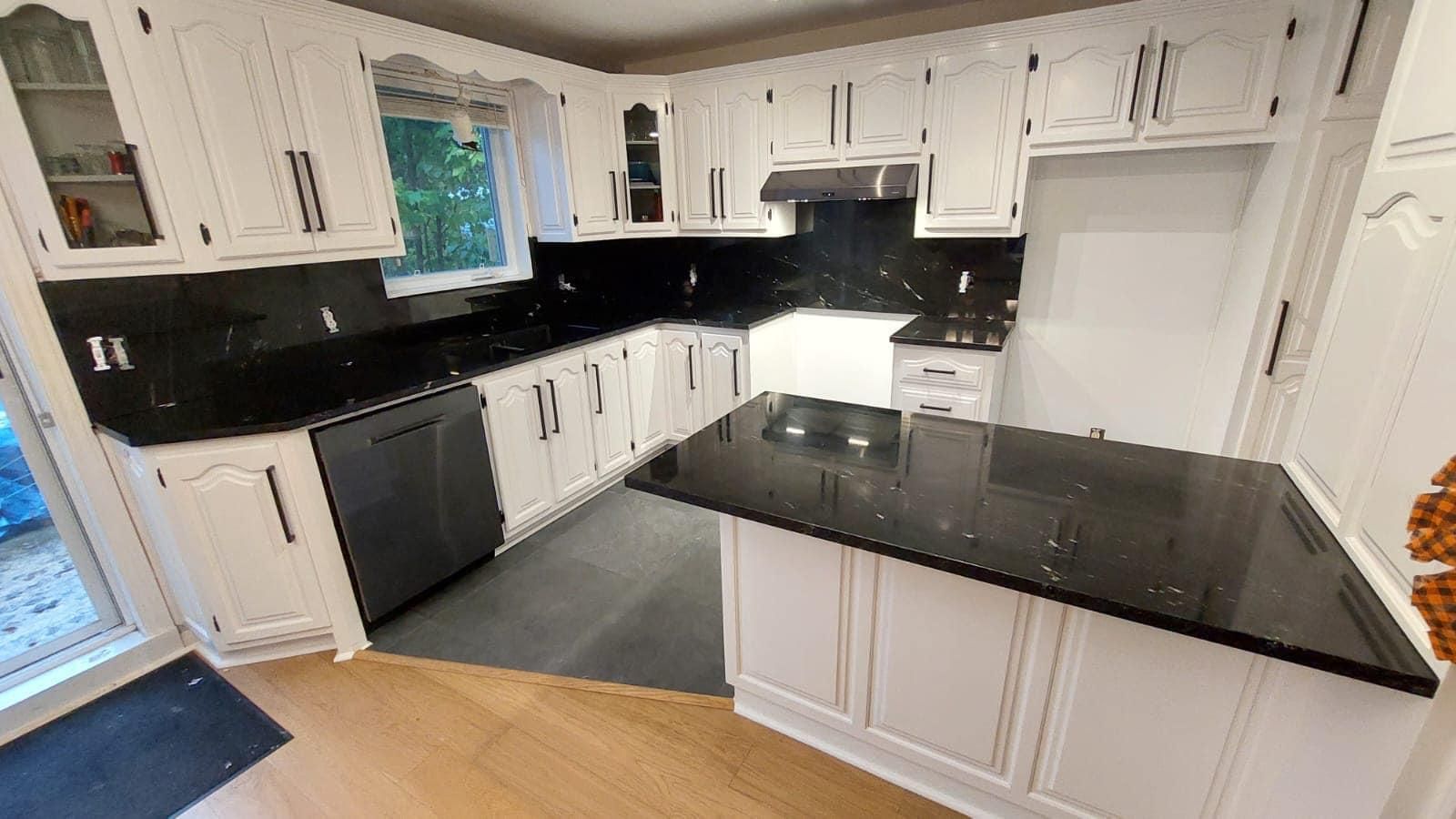 Une cuisine avec des armoires blanches et des comptoirs noirs.
