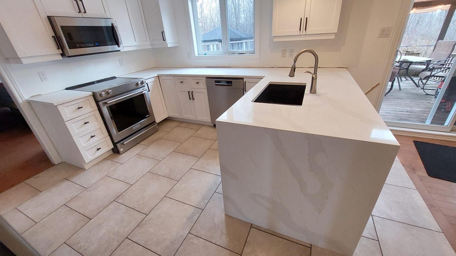 Une cuisine avec des armoires blanches, des appareils électroménagers en acier inoxydable, un évier et un grand îlot.