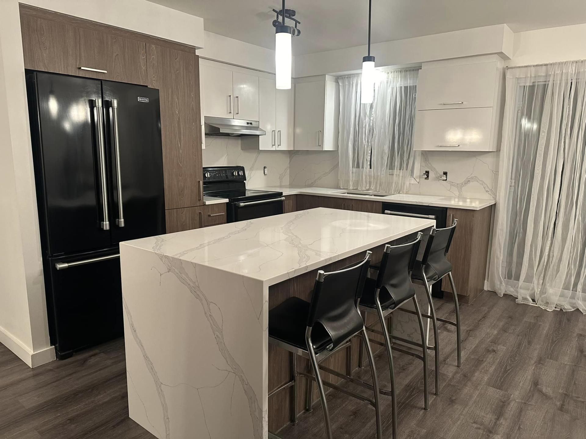 Une cuisine avec un grand îlot et des tabourets et un réfrigérateur noir.