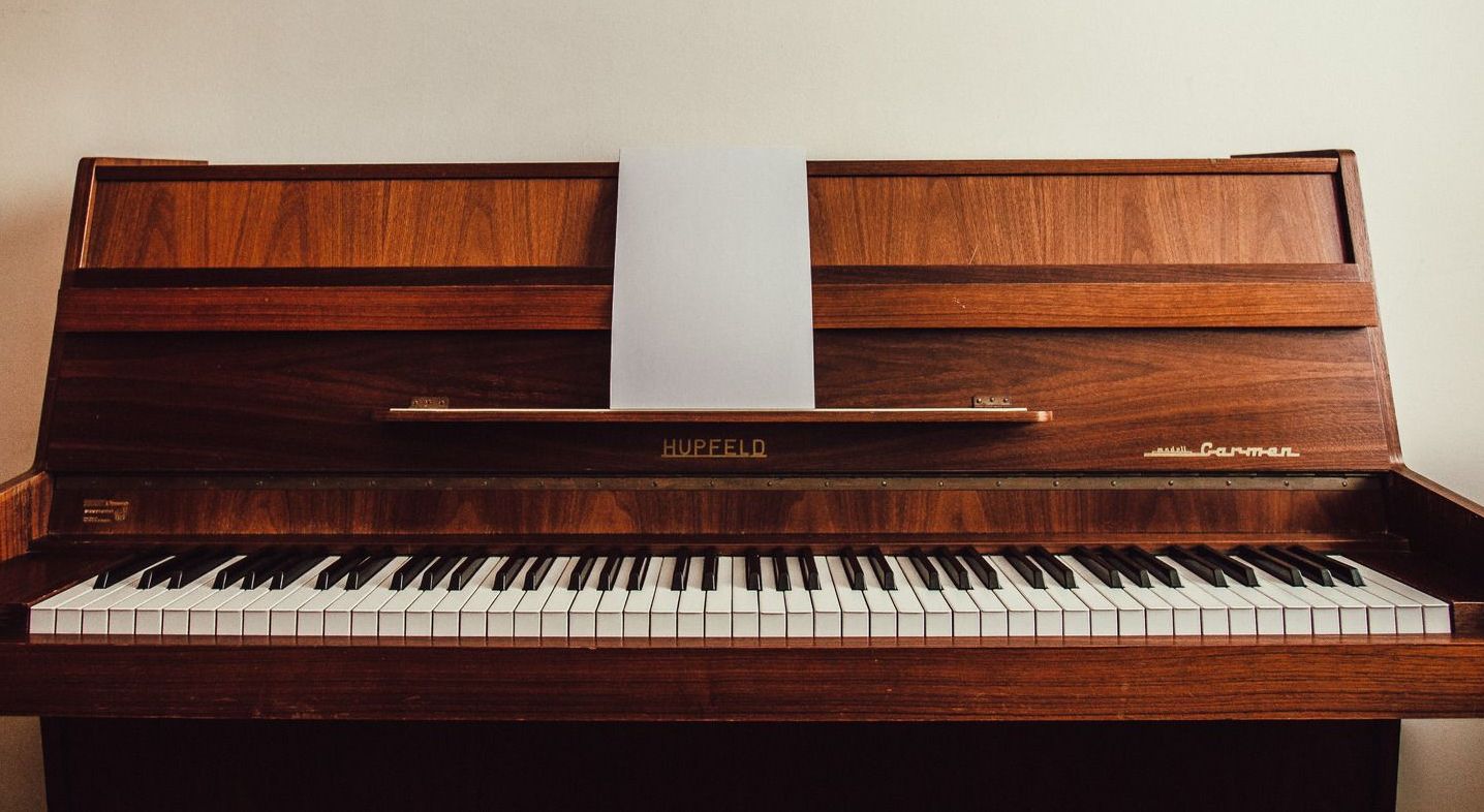A wooden piano is sitting in front of a white wall.