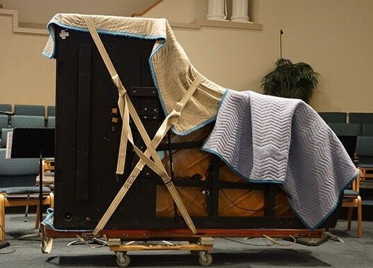 A piano is covered with a blue blanket and straps