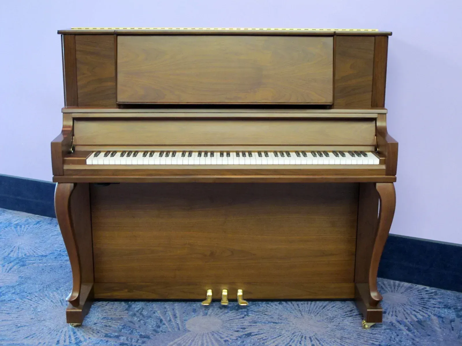 A piano is sitting on a carpet in front of a purple wall