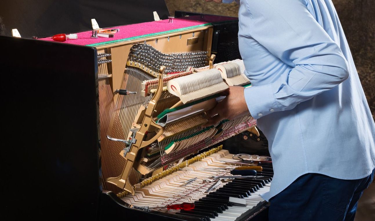 A man in a blue shirt is working on a piano.