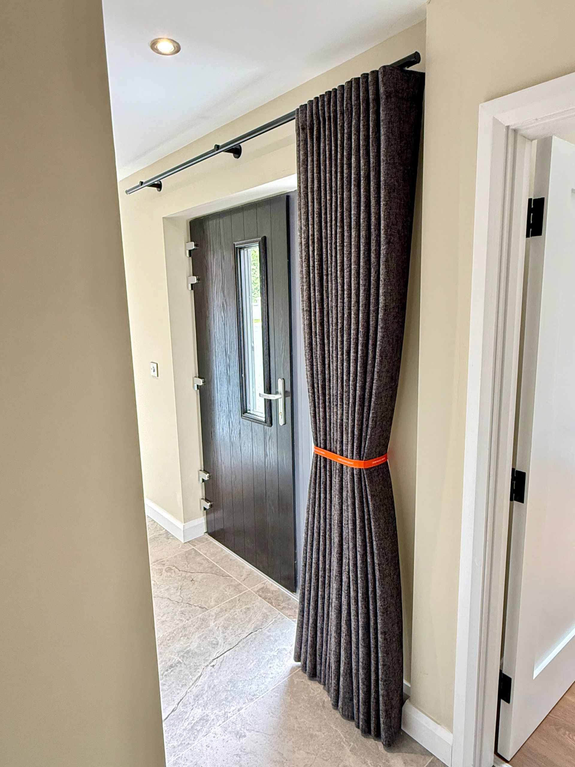 Hallway with a dark wooden door. Brown curtain hangs on the left side, held by an orange tie.