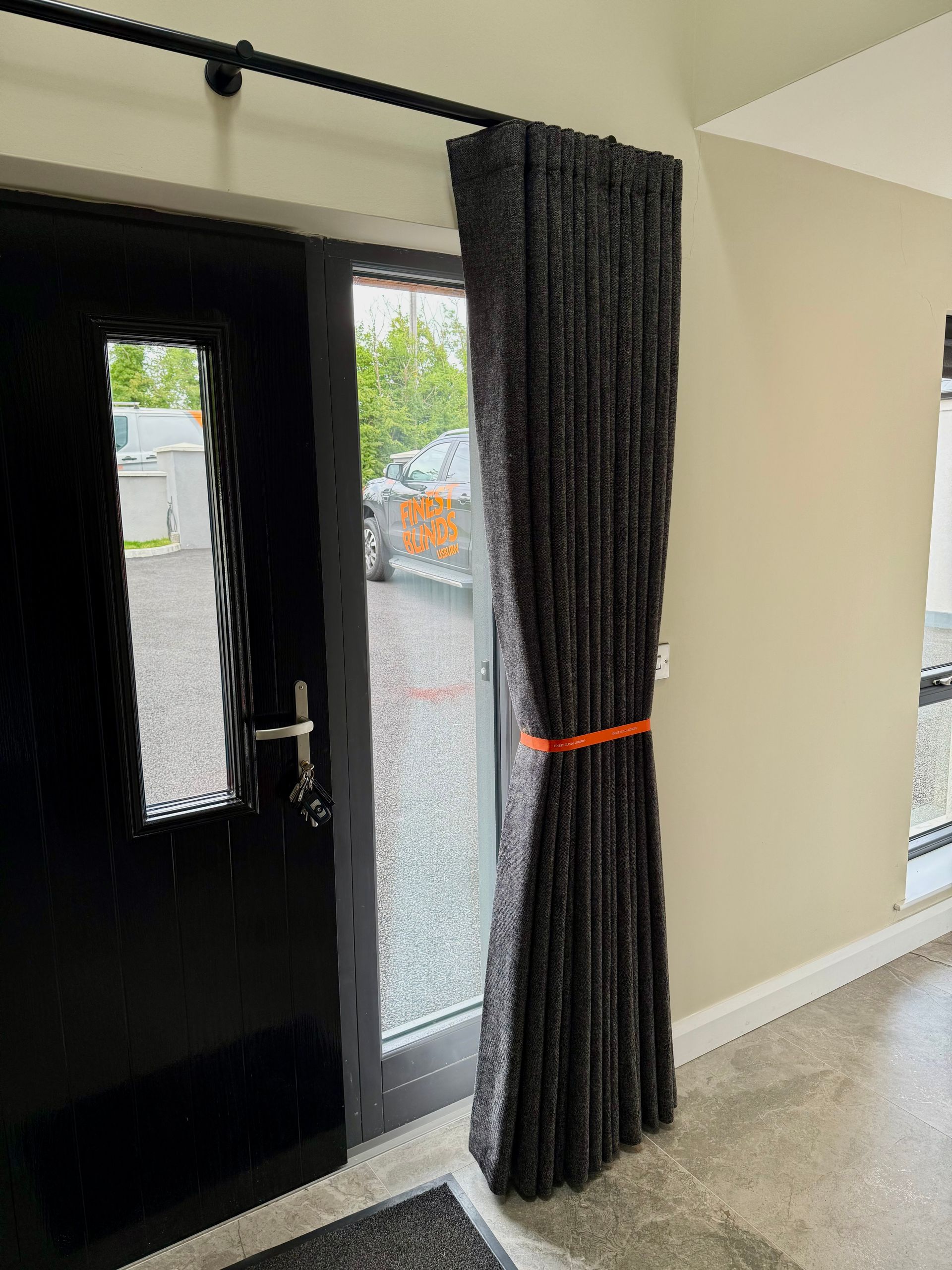Black door with sheer window, dark curtain tied with orange band.
