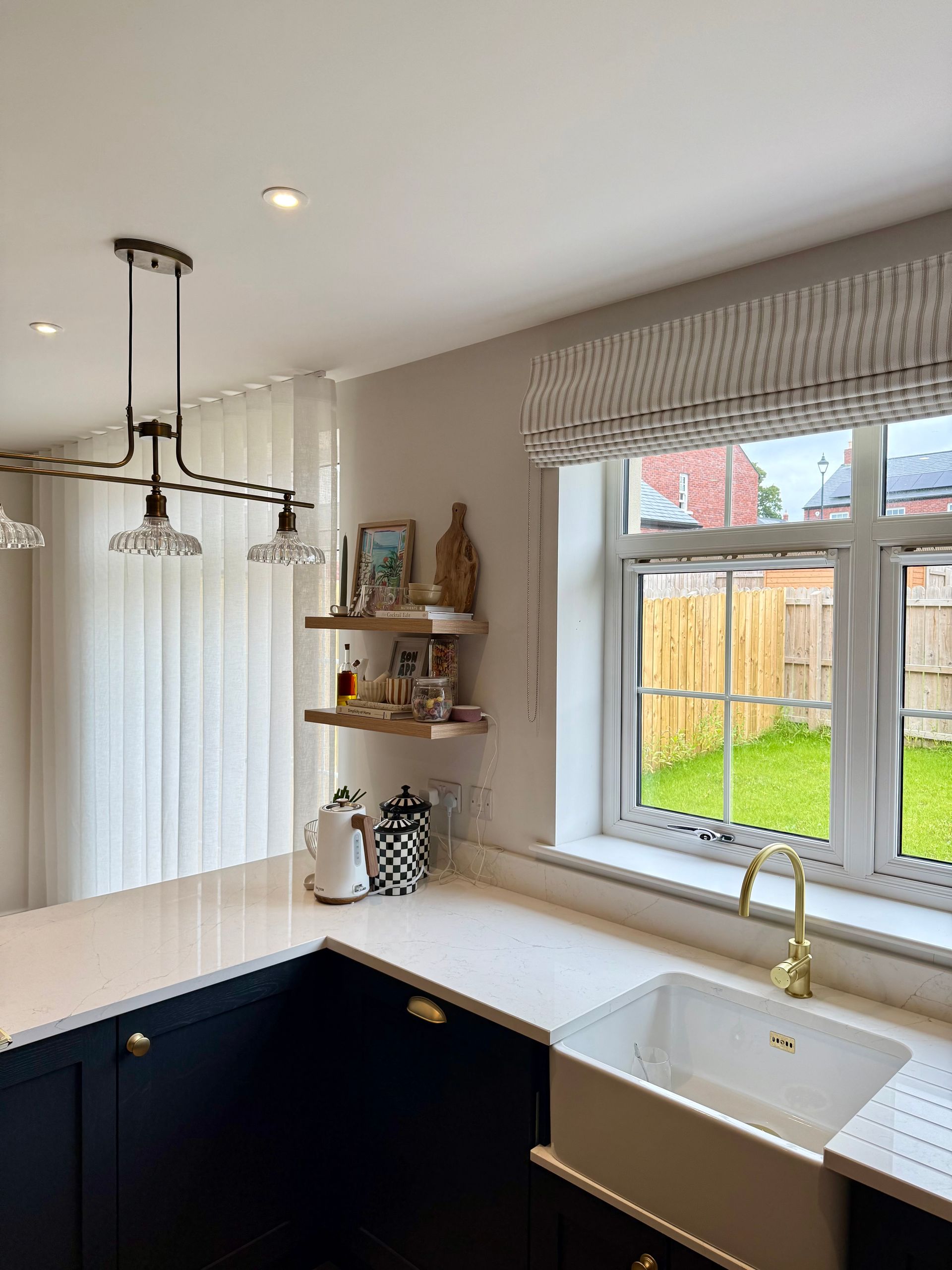 Kitchen with dark blue cabinets, white countertop, sink, and window with blinds.