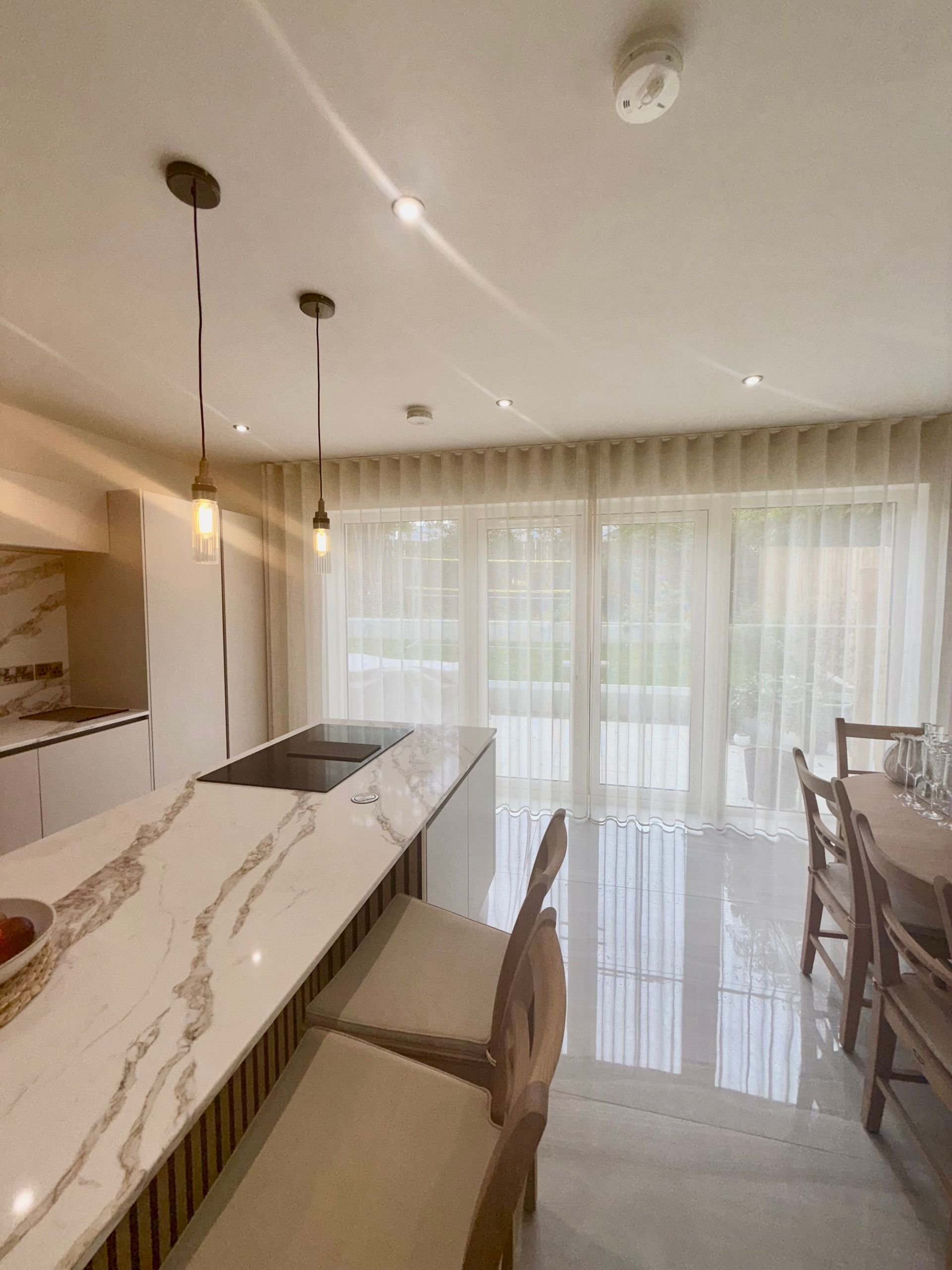 Modern kitchen with a marble island, bar stools, and sheer curtains.