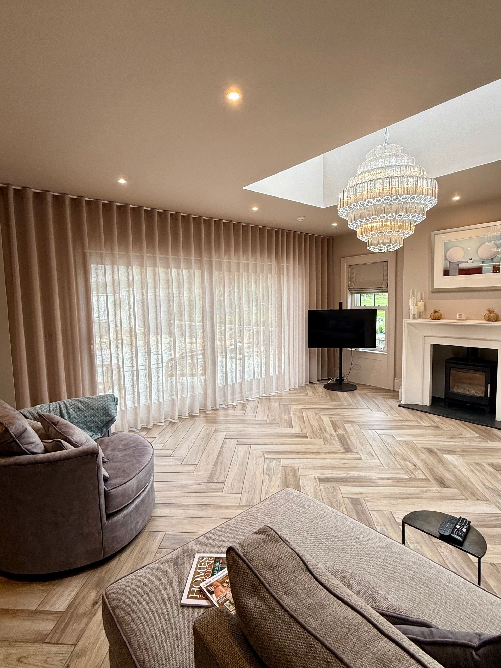 Living room with curved wall, patterned wood floor, crystal chandelier, and large window.