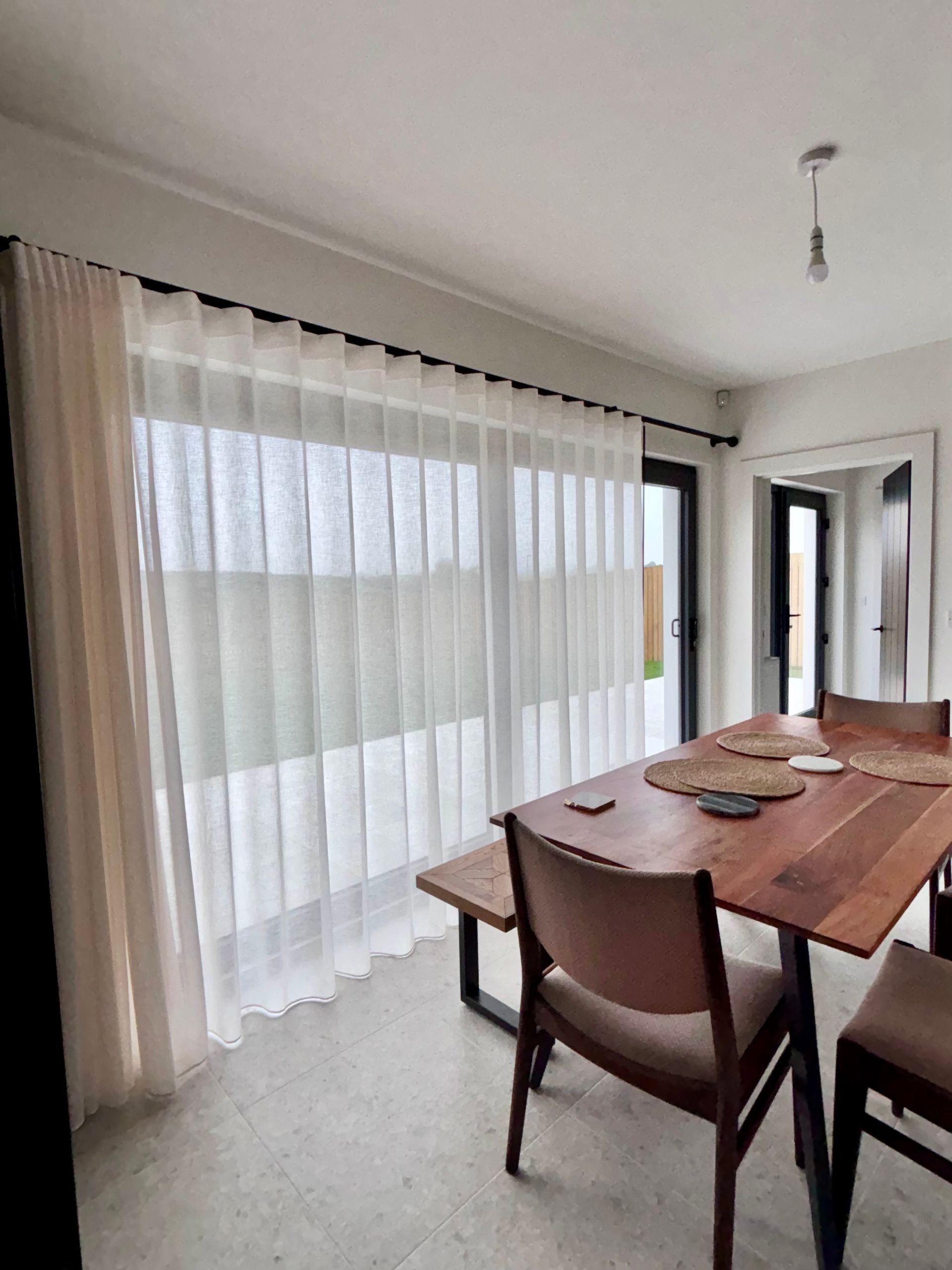 Dining room with sheer white curtains, wood table, black window frames.