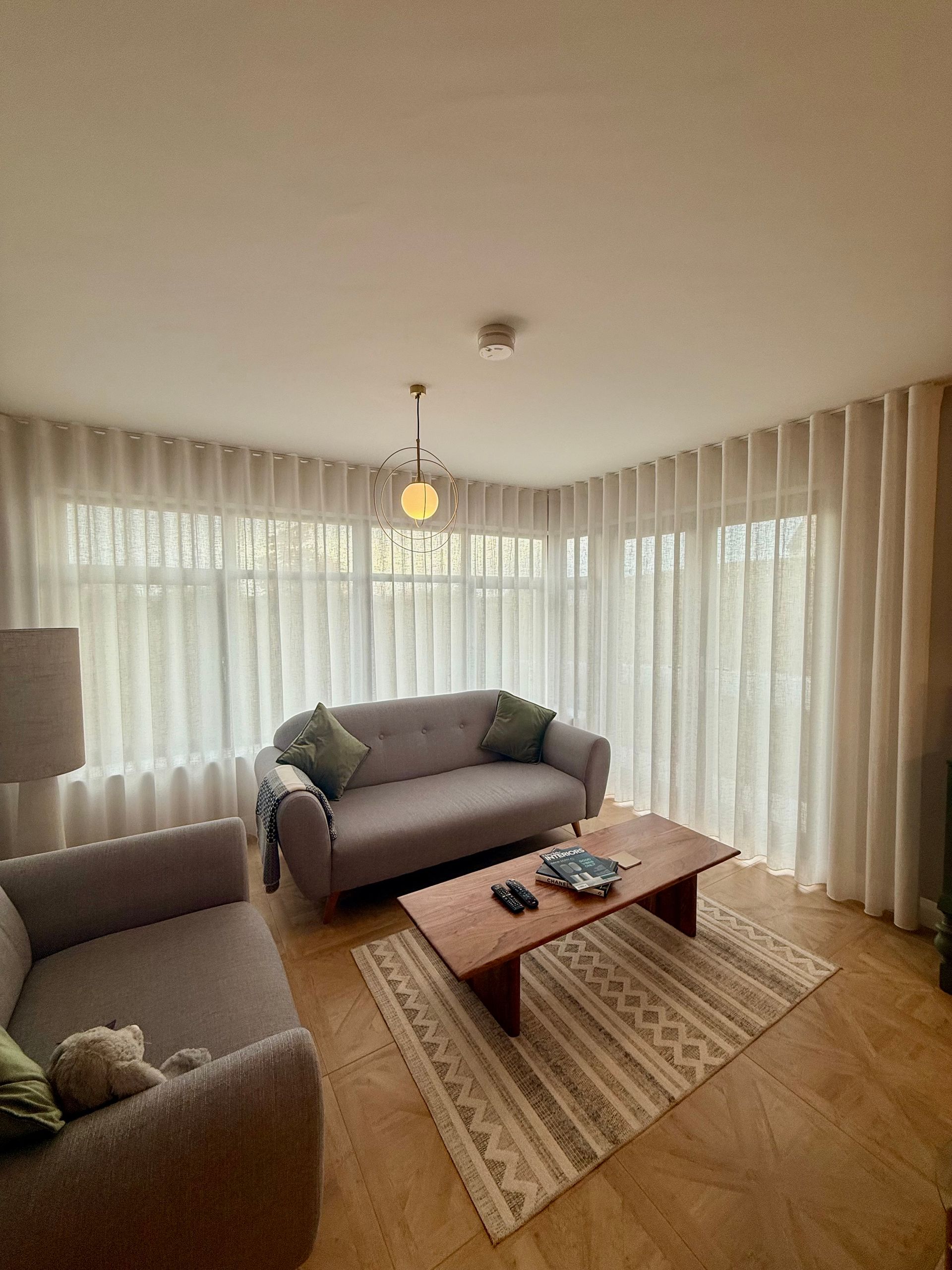 Living room with neutral tones, two gray sofas, white curtains, and a wooden coffee table.