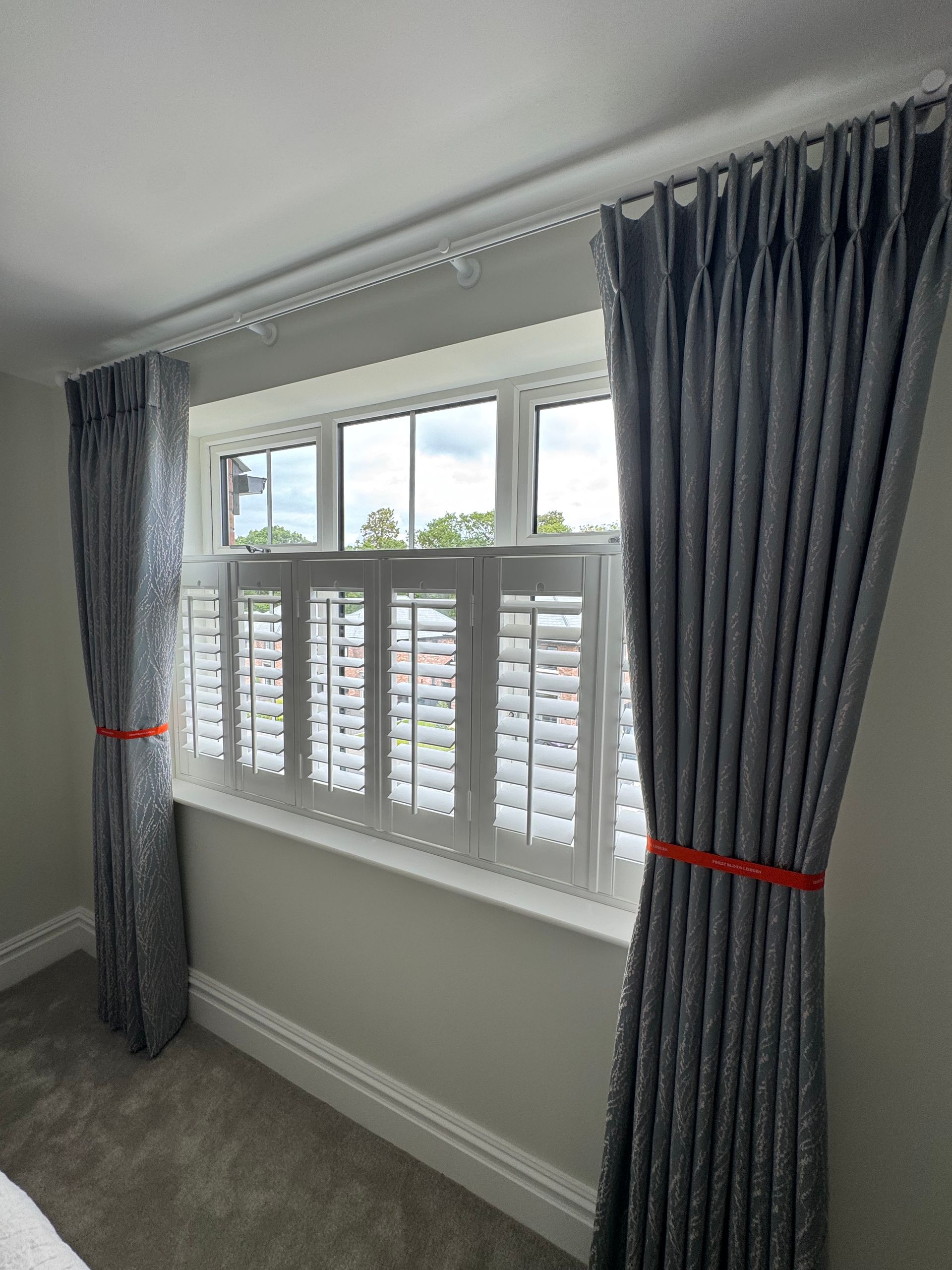 Window with white shutters and gray curtains, tied with orange bands.