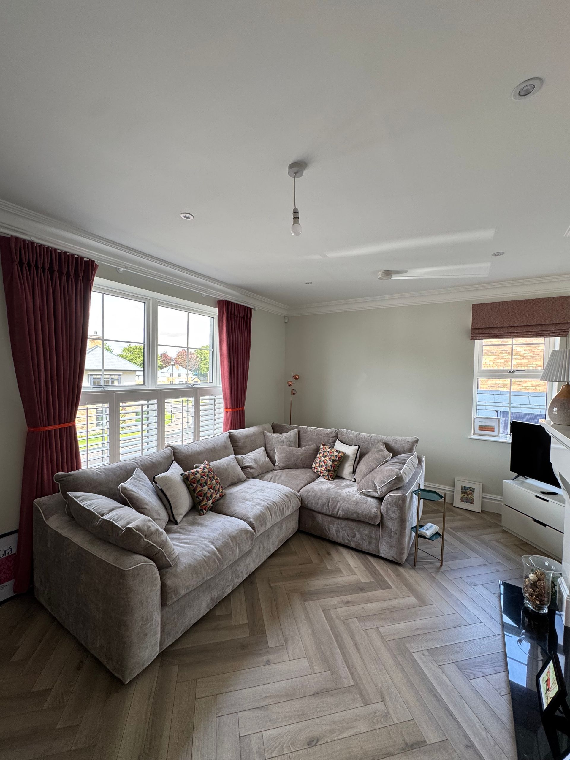 Living room with sectional sofa, herringbone floors, and burgundy curtains.