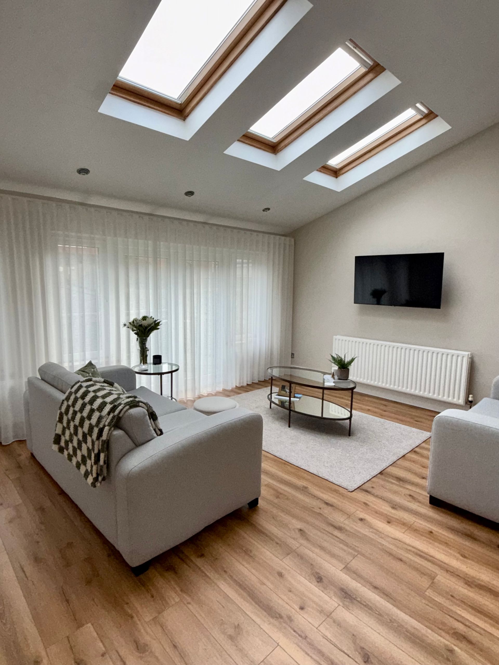Living room with skylights, gray sofas, wooden floor, and a TV on the wall.
