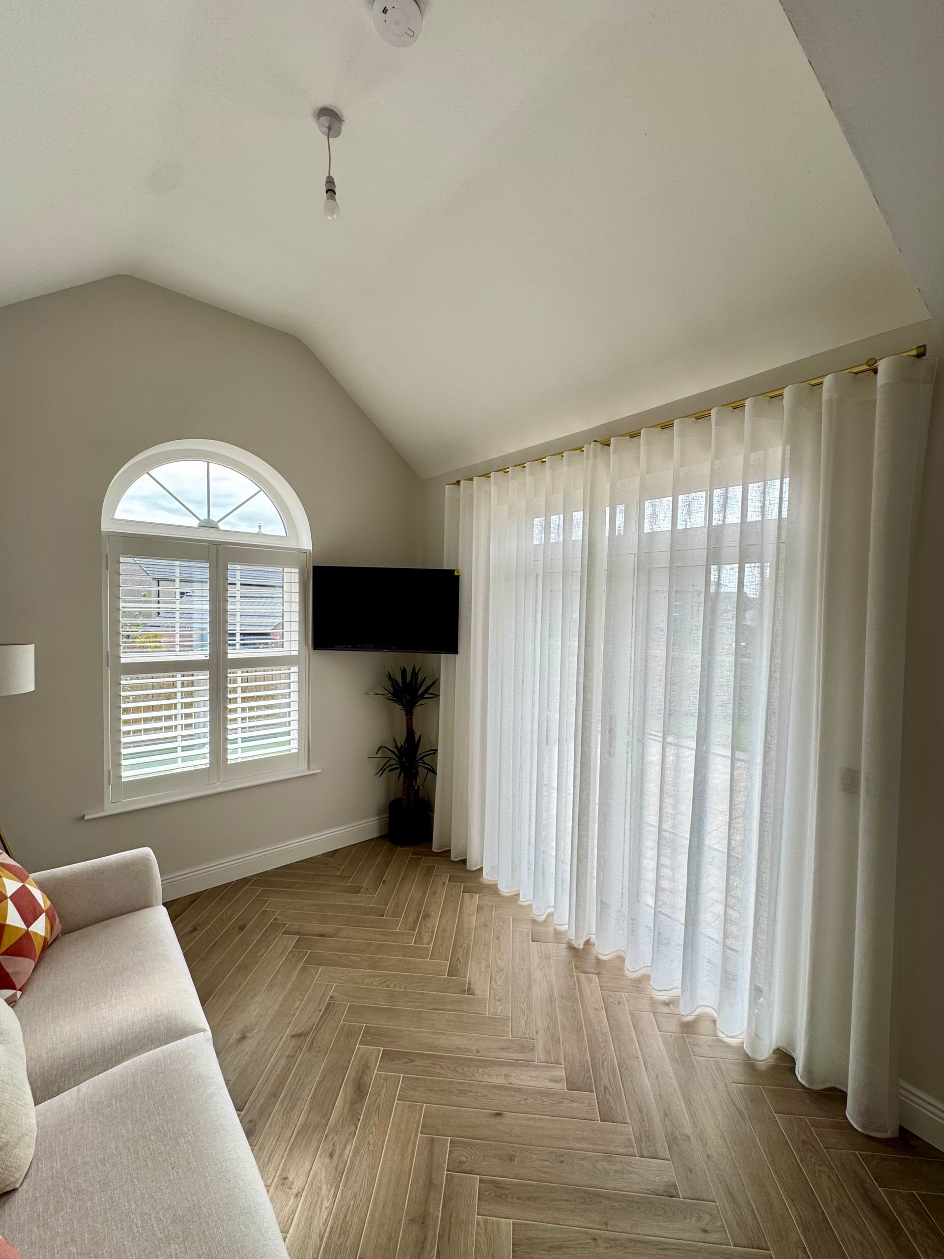 Living room with arched window and sheer white curtains over door. Beige couch and herringbone floor.