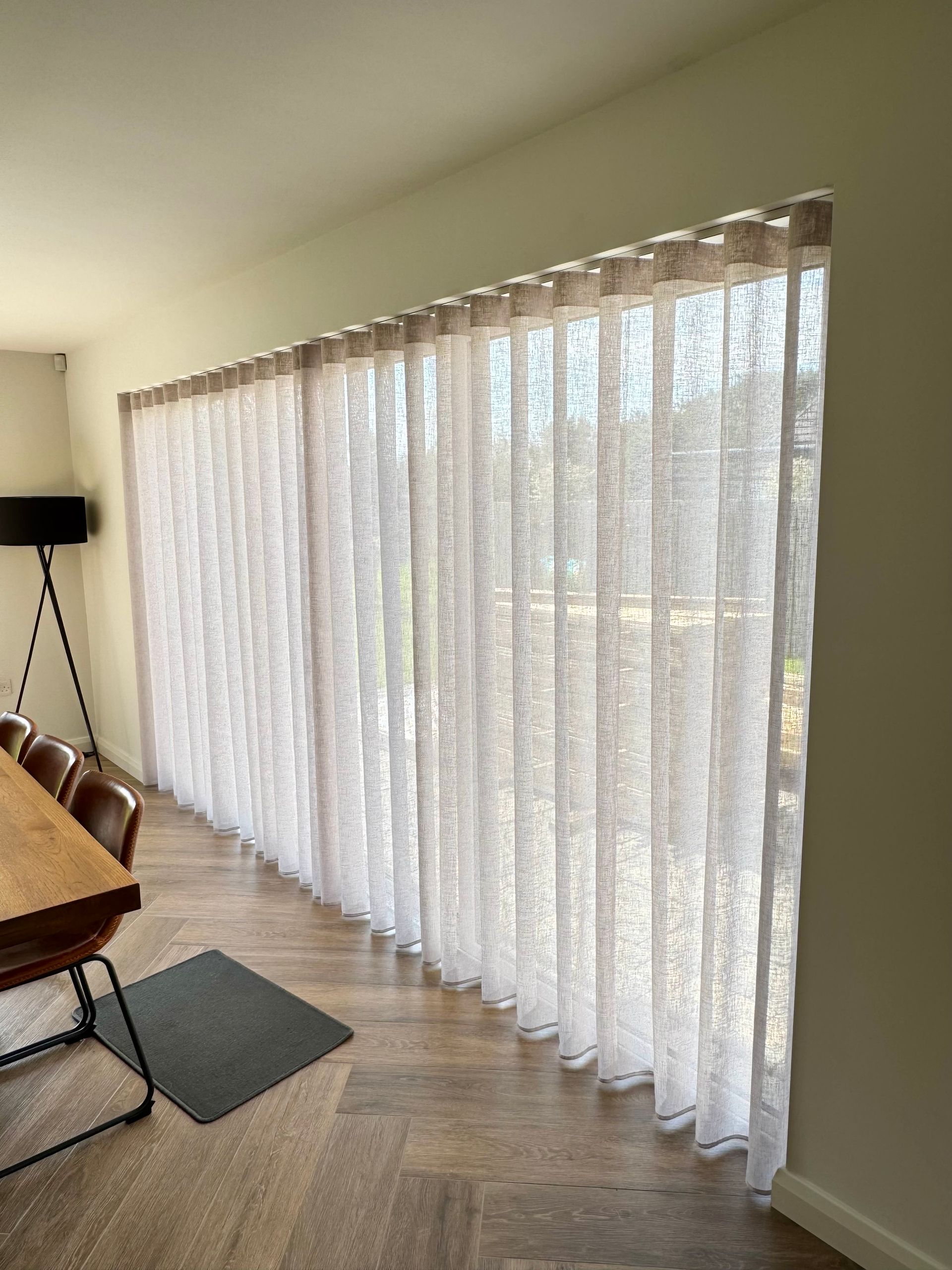 Sheer white curtains on large window in a dining area.