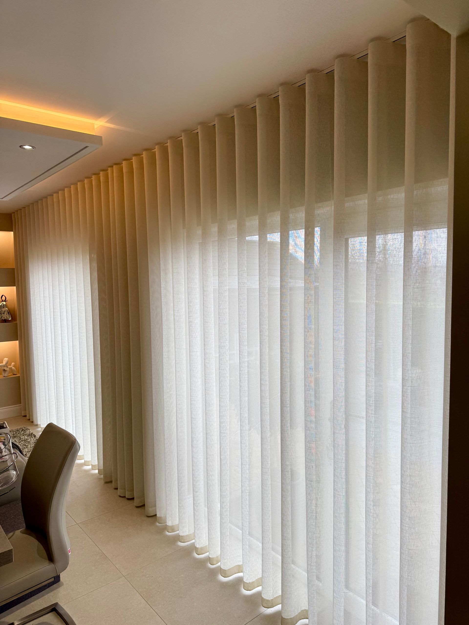 Light cream-colored curtains hang in front of a window. A chair is visible in the foreground.