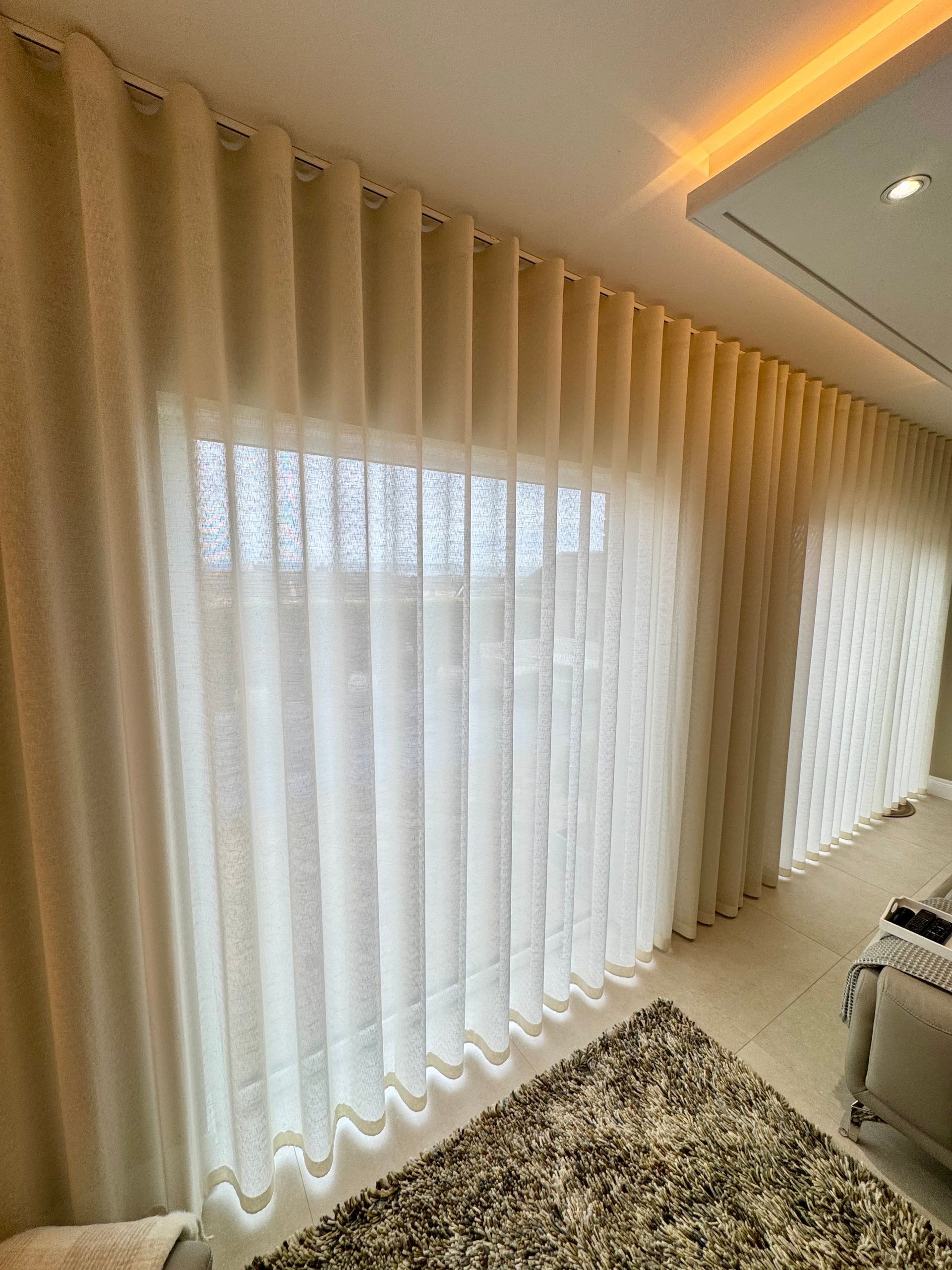 Light beige, full-length curtains in a modern room, covering a window. A patterned rug is on the floor.