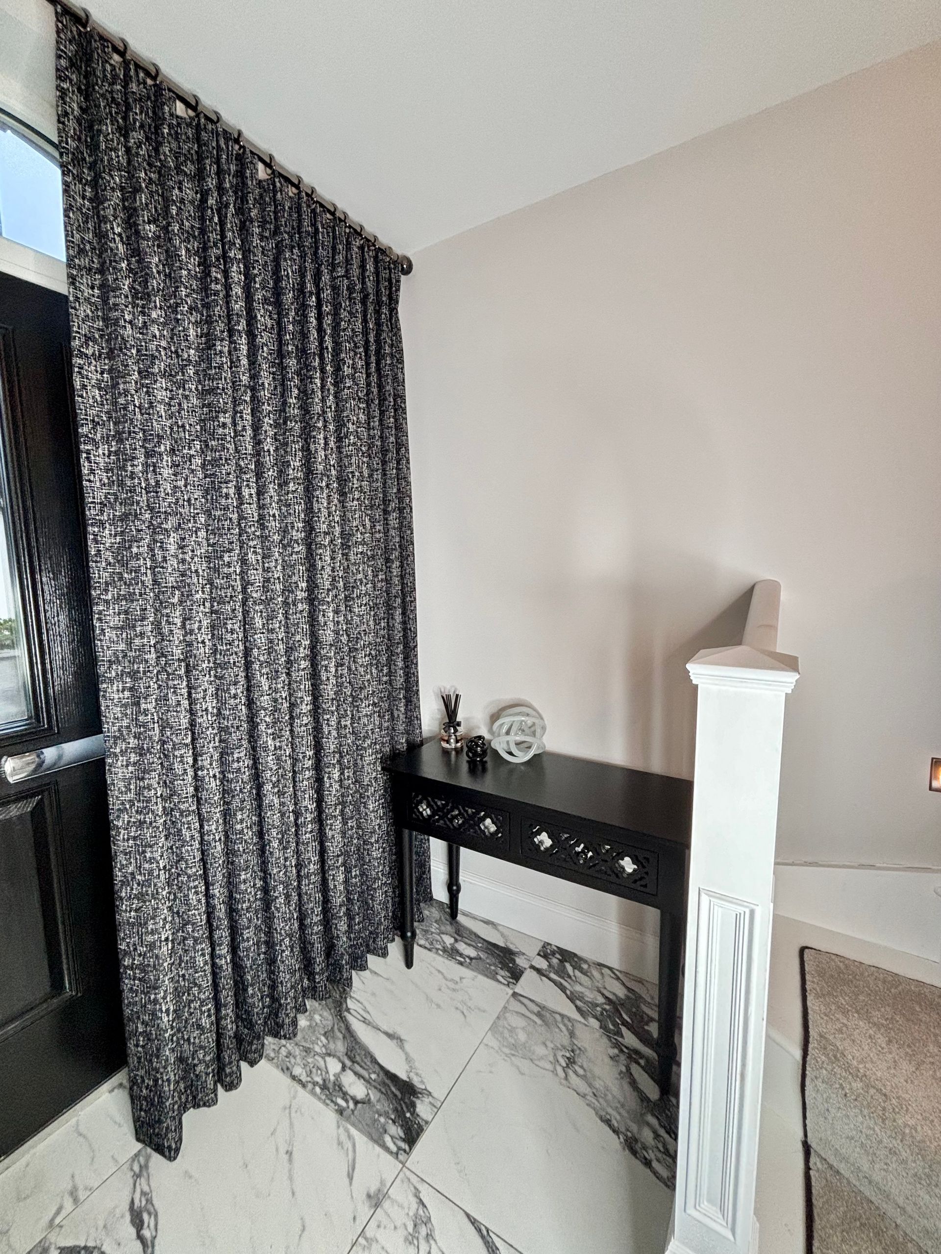 Black and white patterned curtains beside a black table on a marble floor. White wall and pillar.