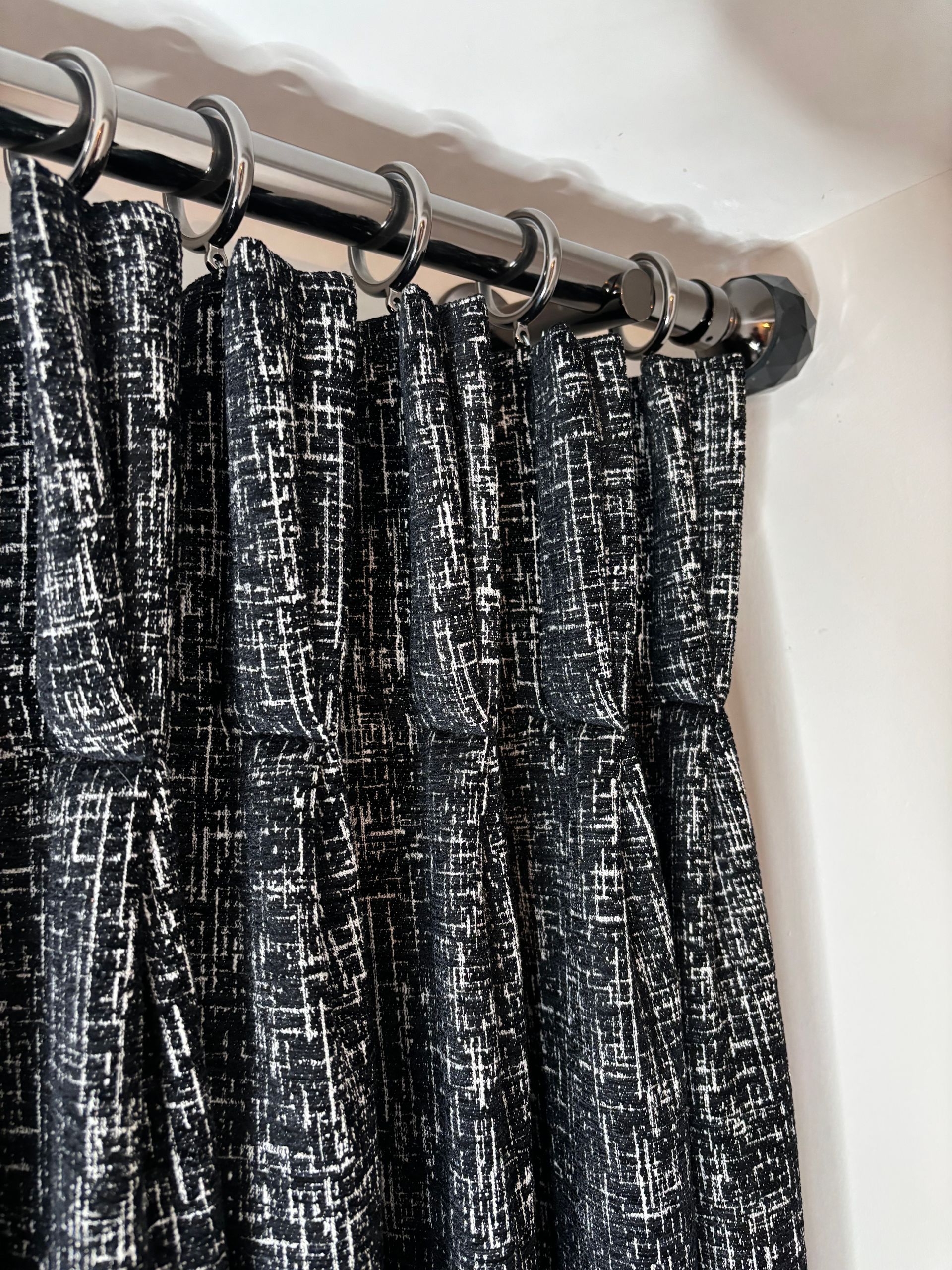 Black and white patterned curtain hanging from silver rings on a rod, against a white wall.