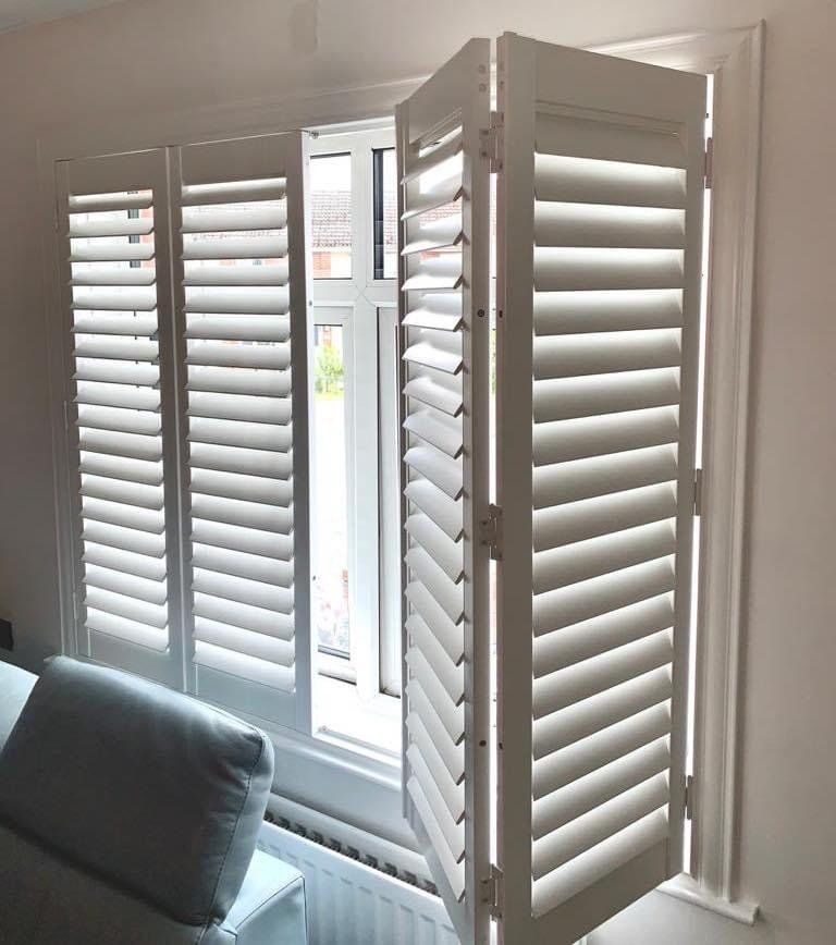 A living room with white shutters on the windows and a couch.