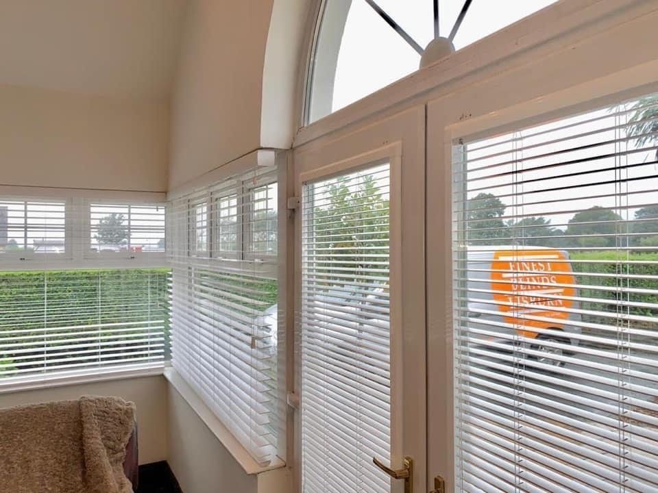 A living room with blinds on the windows and a chair.