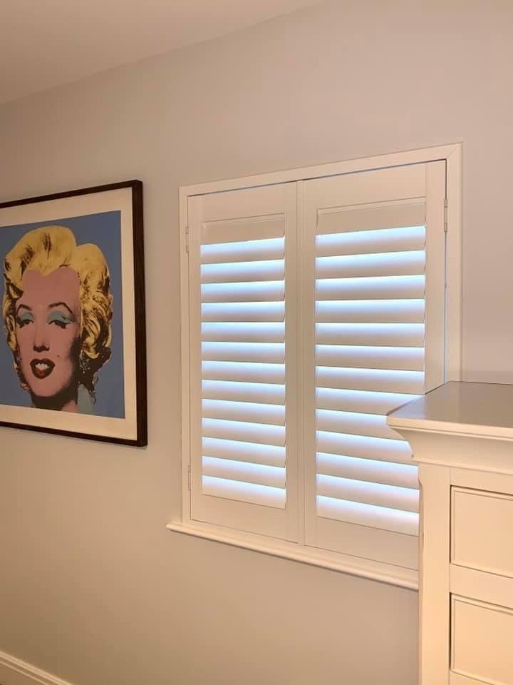 There is a painting of marilyn monroe on the wall next to a window with shutters.